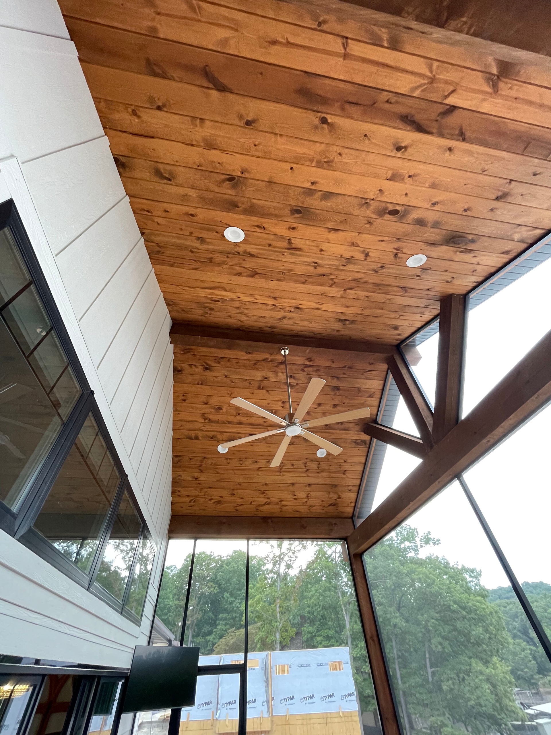 Wooden covered patio ceiling with a large ceiling fan and open sides overlooking trees