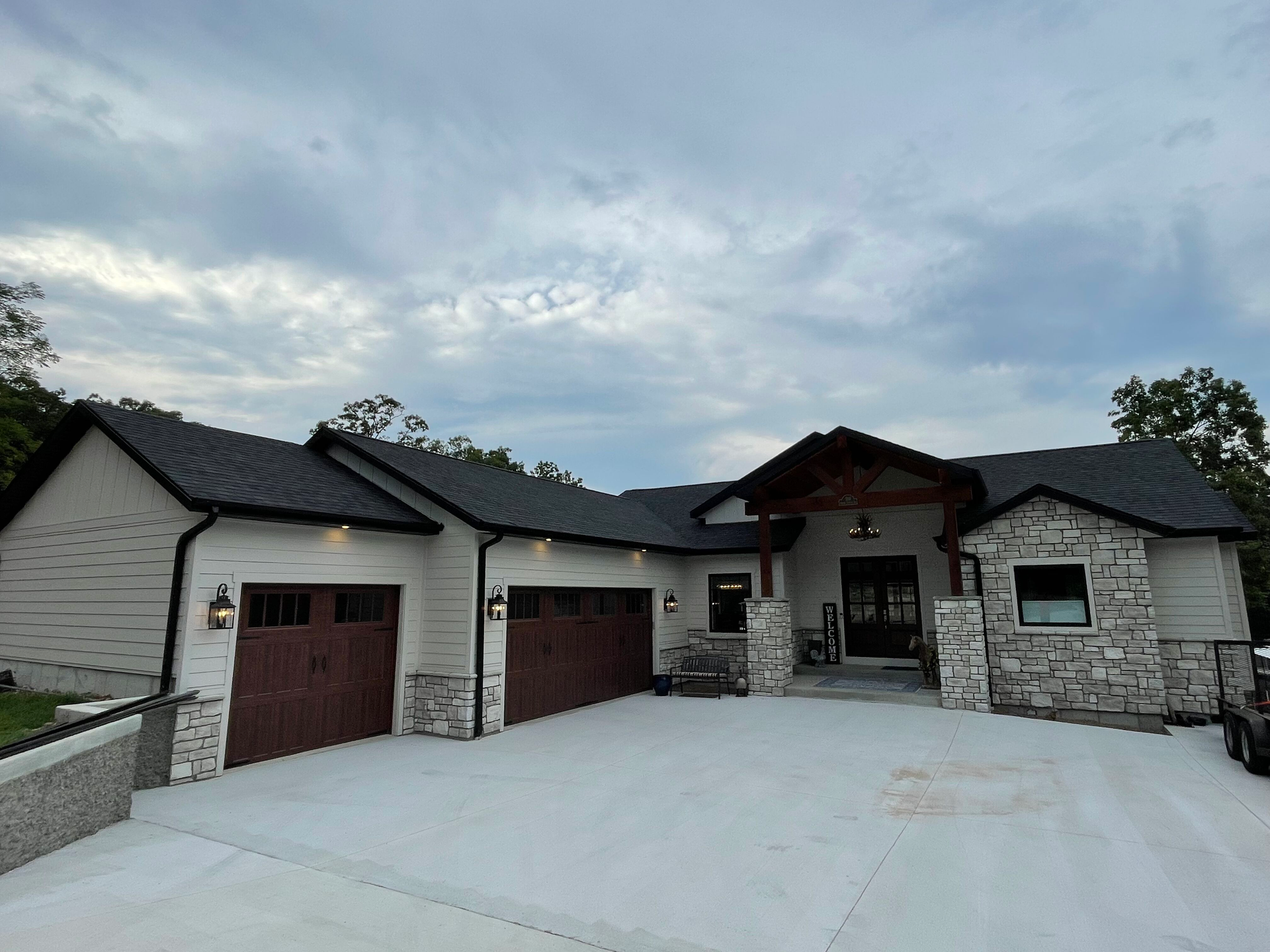 Modern single-story stone house with three garage doors and a wide concrete driveway under a cloudy sky
