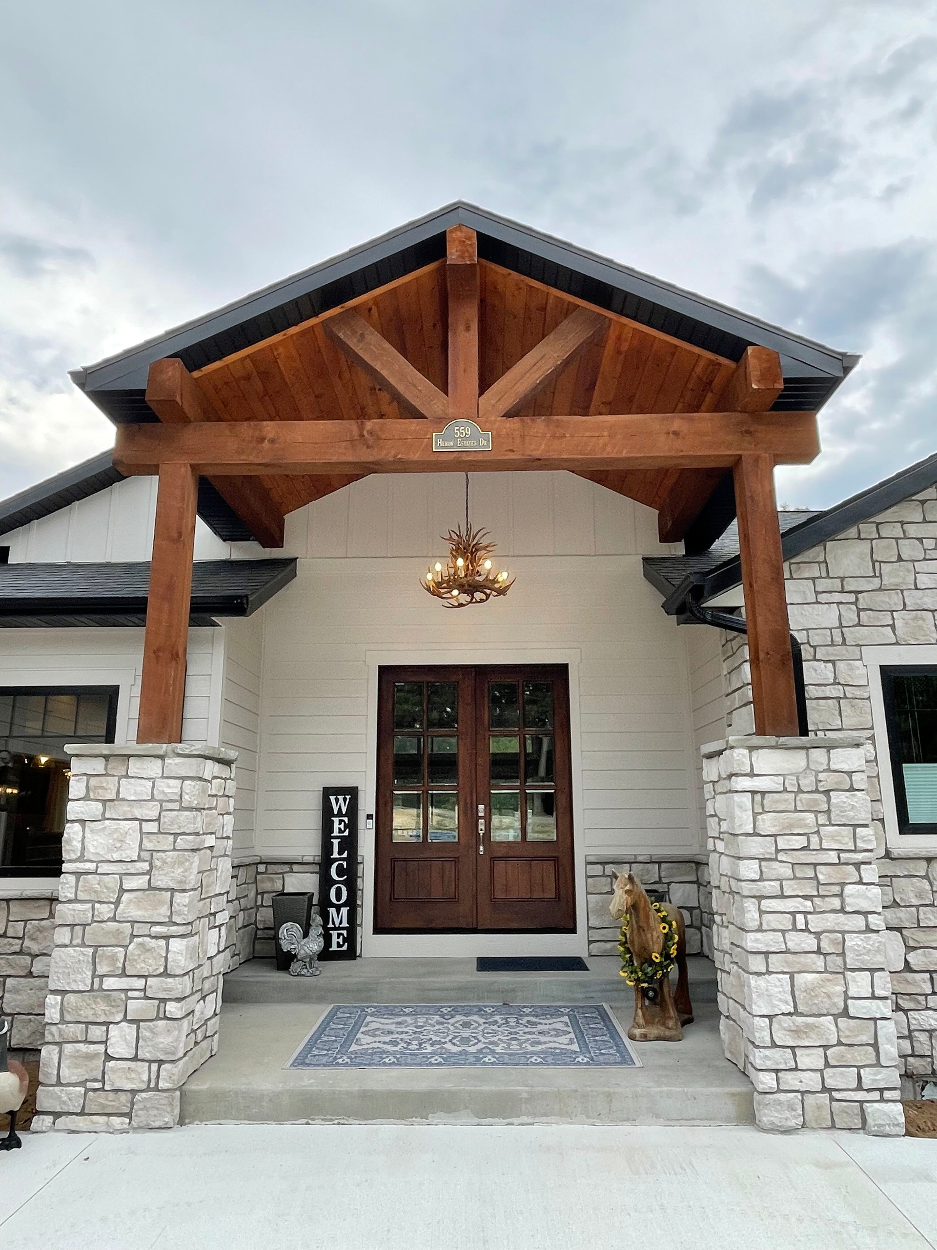 Stone house entryway with wooden gabled porch, front door, and hanging chandelier
