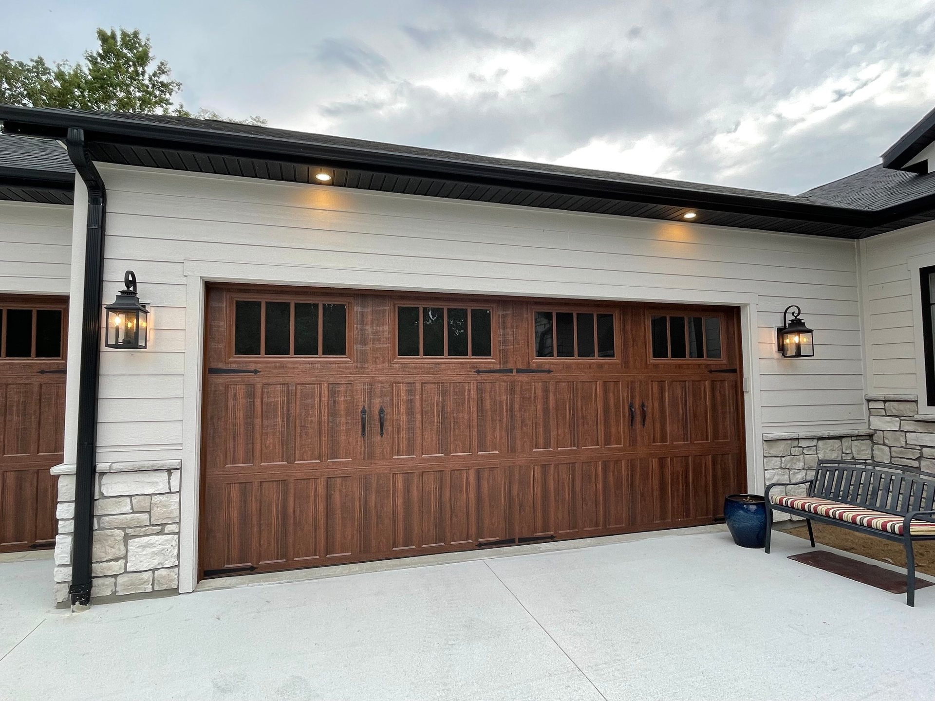 Wooden garage door on a white stucco home with stone trim and wall lanterns
