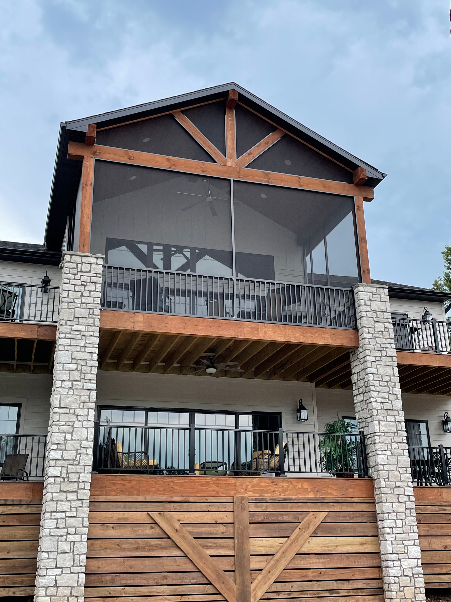 Modern house facade with stone columns, wood accents, and a second-floor balcony under a tiled roof