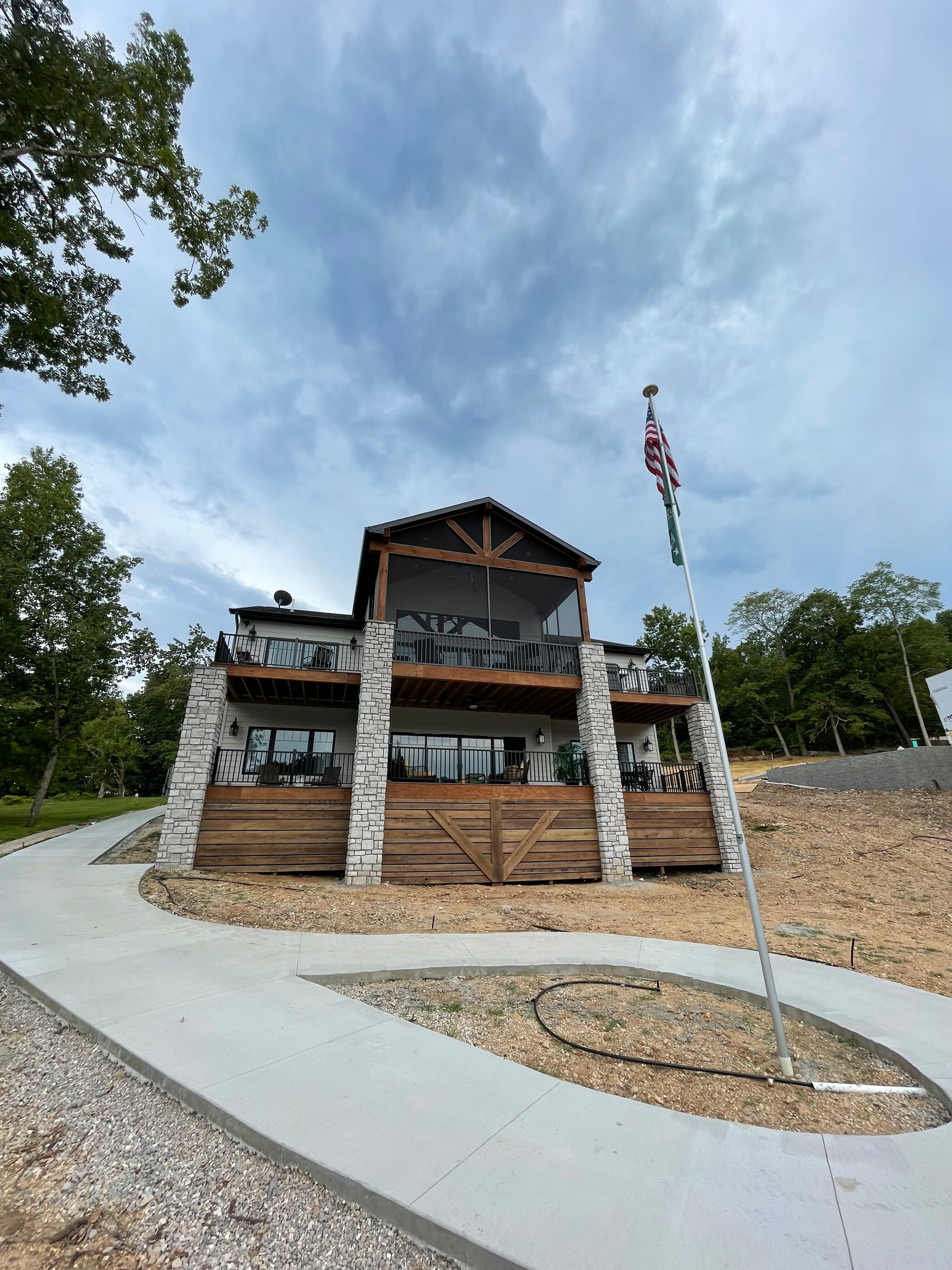 Rustic cabin-style building with stone and wood exterior, flagpole, and curved driveway under a cloudy sky
