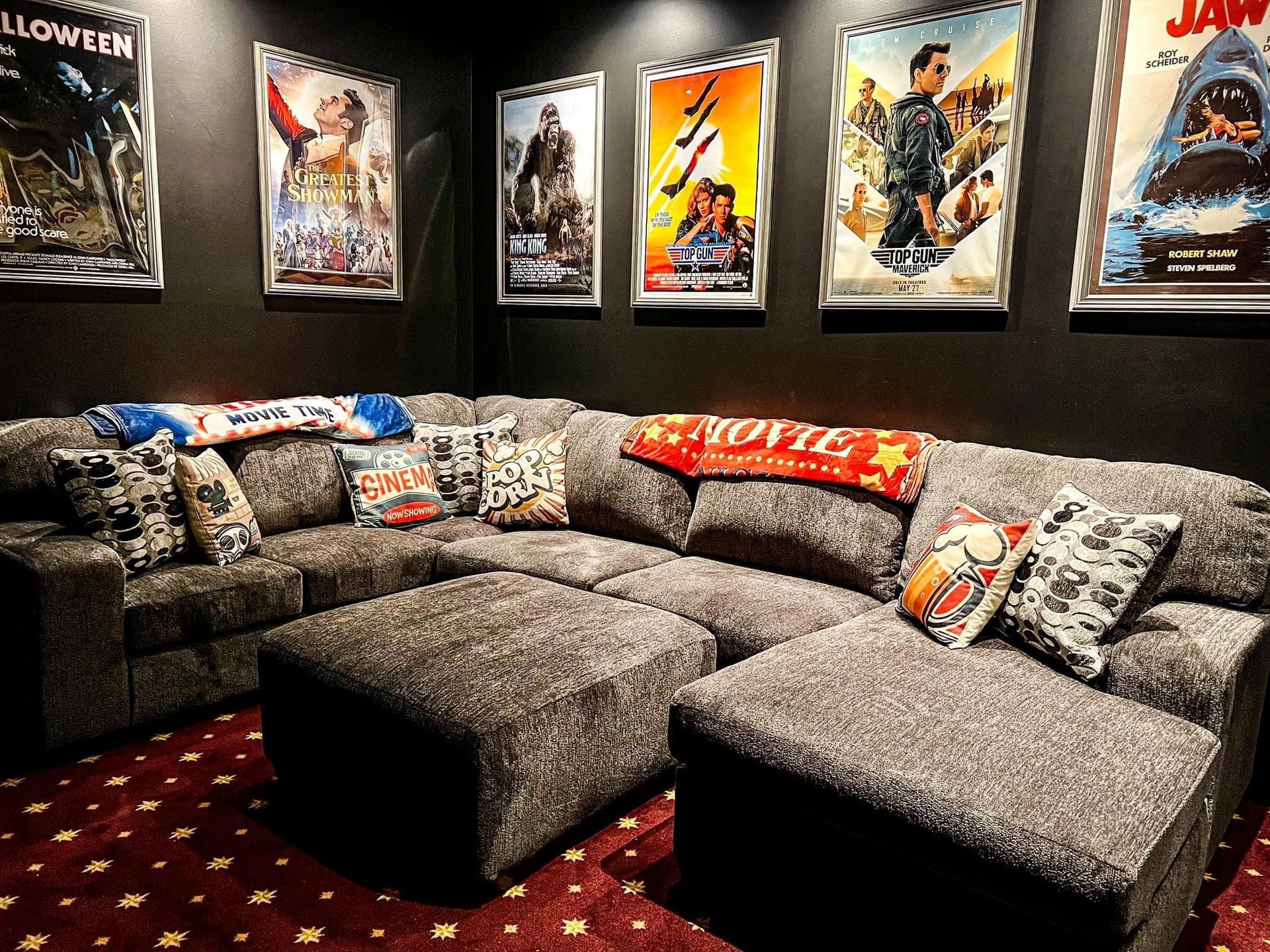 Cozy home theater with gray sectional sofa, colorful throw blankets, and movie posters on black walls