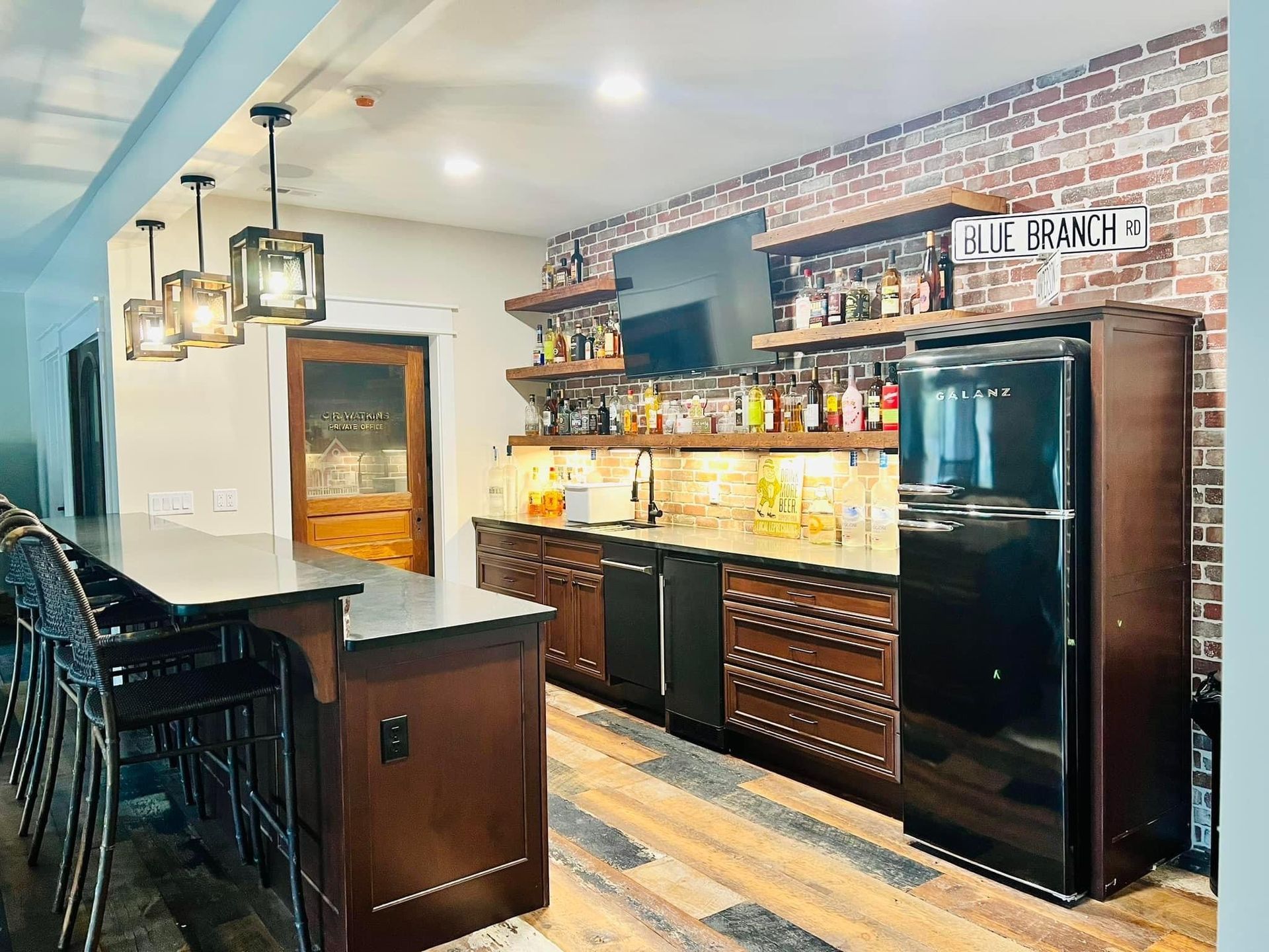 Modern home bar with black cabinets, brick backsplash, shelves, and a black refrigerator in a kitchen space