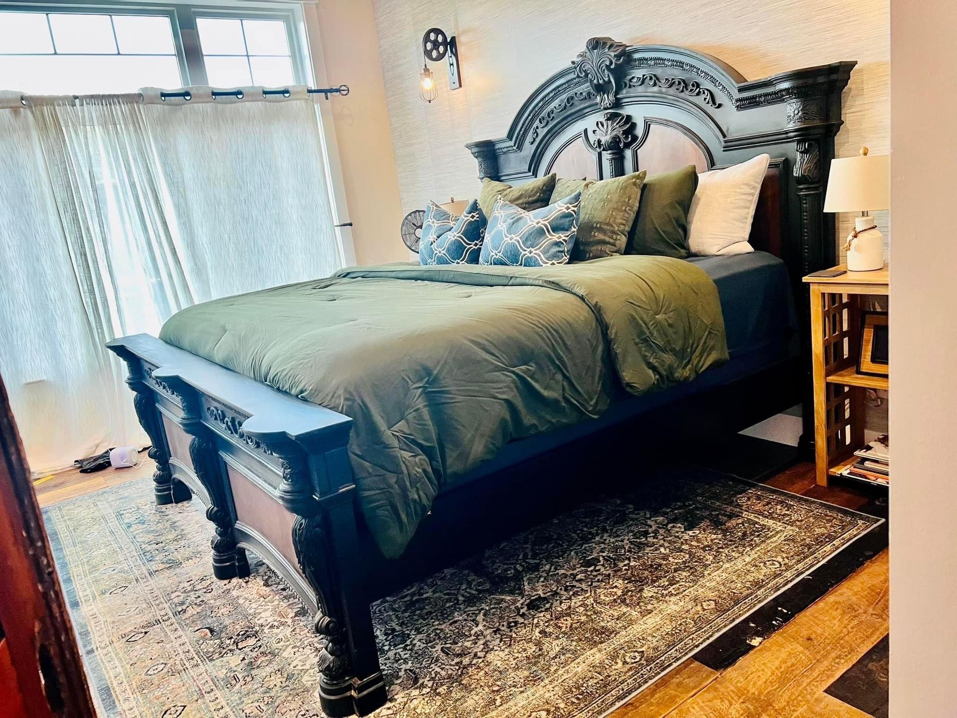 Dark wood bed with ornate headboard, gray bedding, and bedside lamp in a bright bedroom