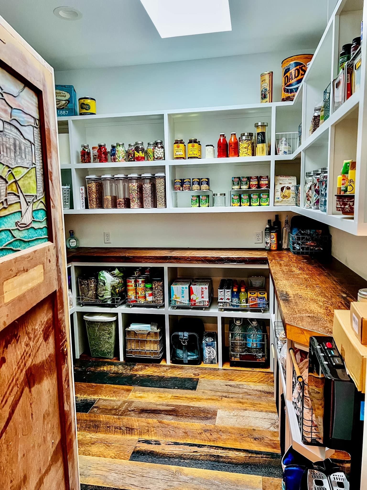 Pantry with white shelves, wood floor, and neatly stocked jars, cans, and snacks on both sides.