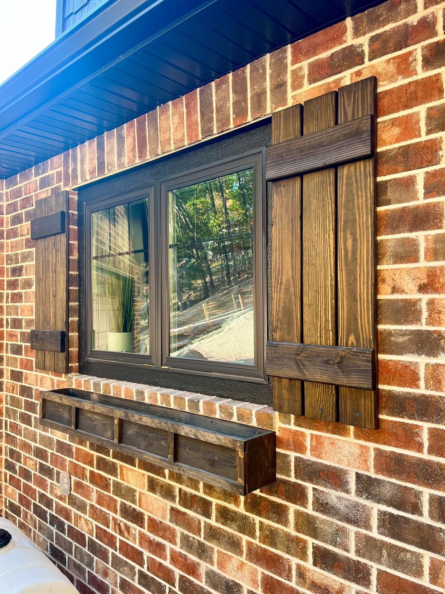 Brick house wall with a black-framed window, wooden shutters, and a small ledge under the sill