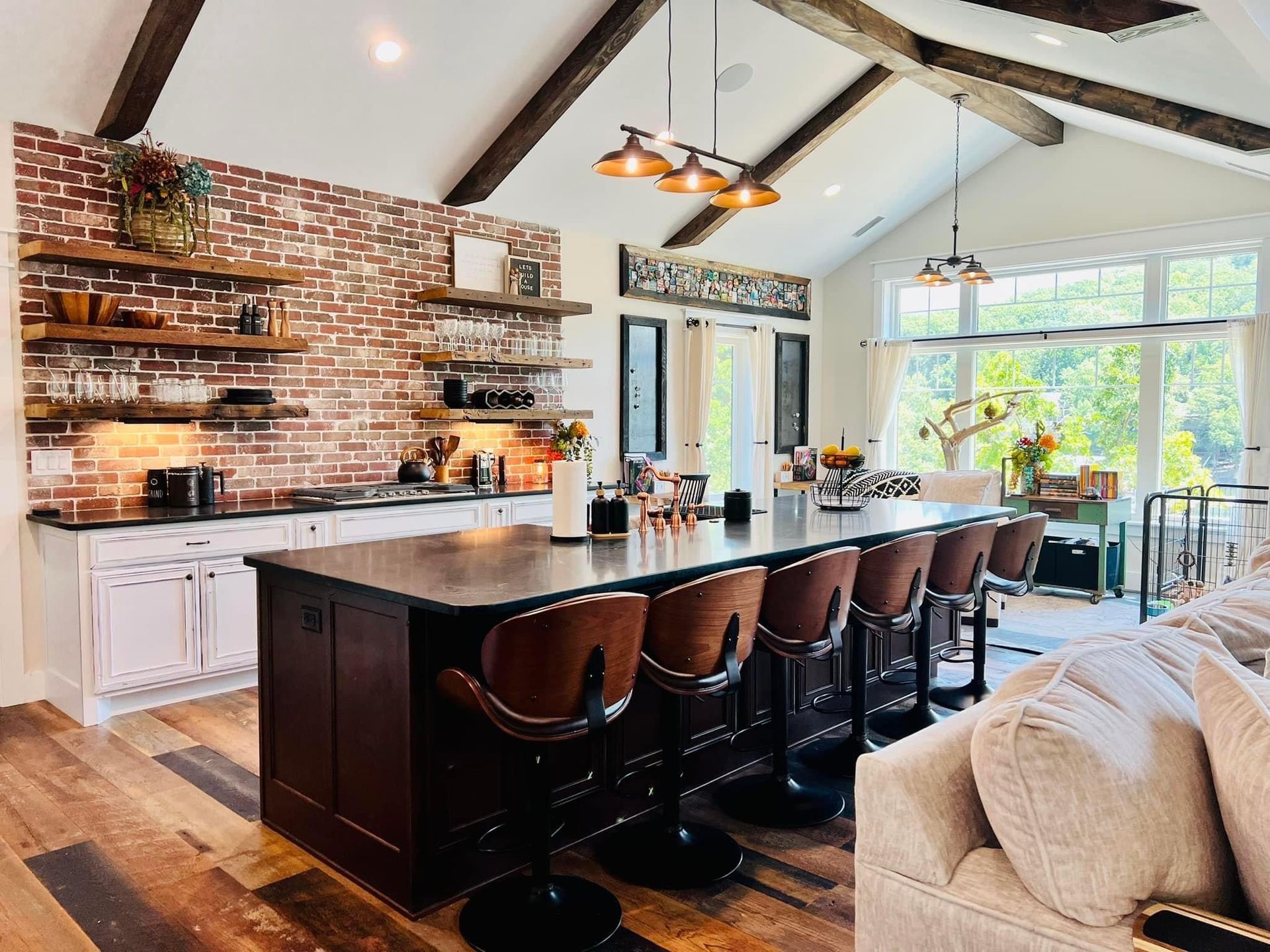 Spacious kitchen with brick accent wall, dark island stools, and large windows overlooking a bright dining area