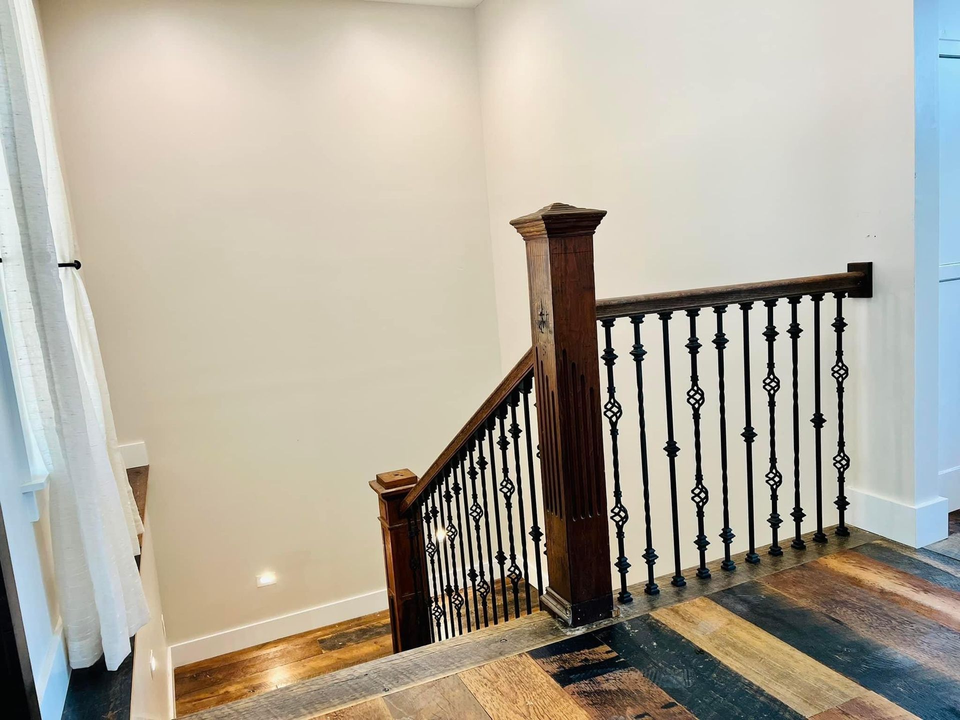 Staircase landing with wooden handrail, dark balusters, and striped carpet in a bright interior hallway