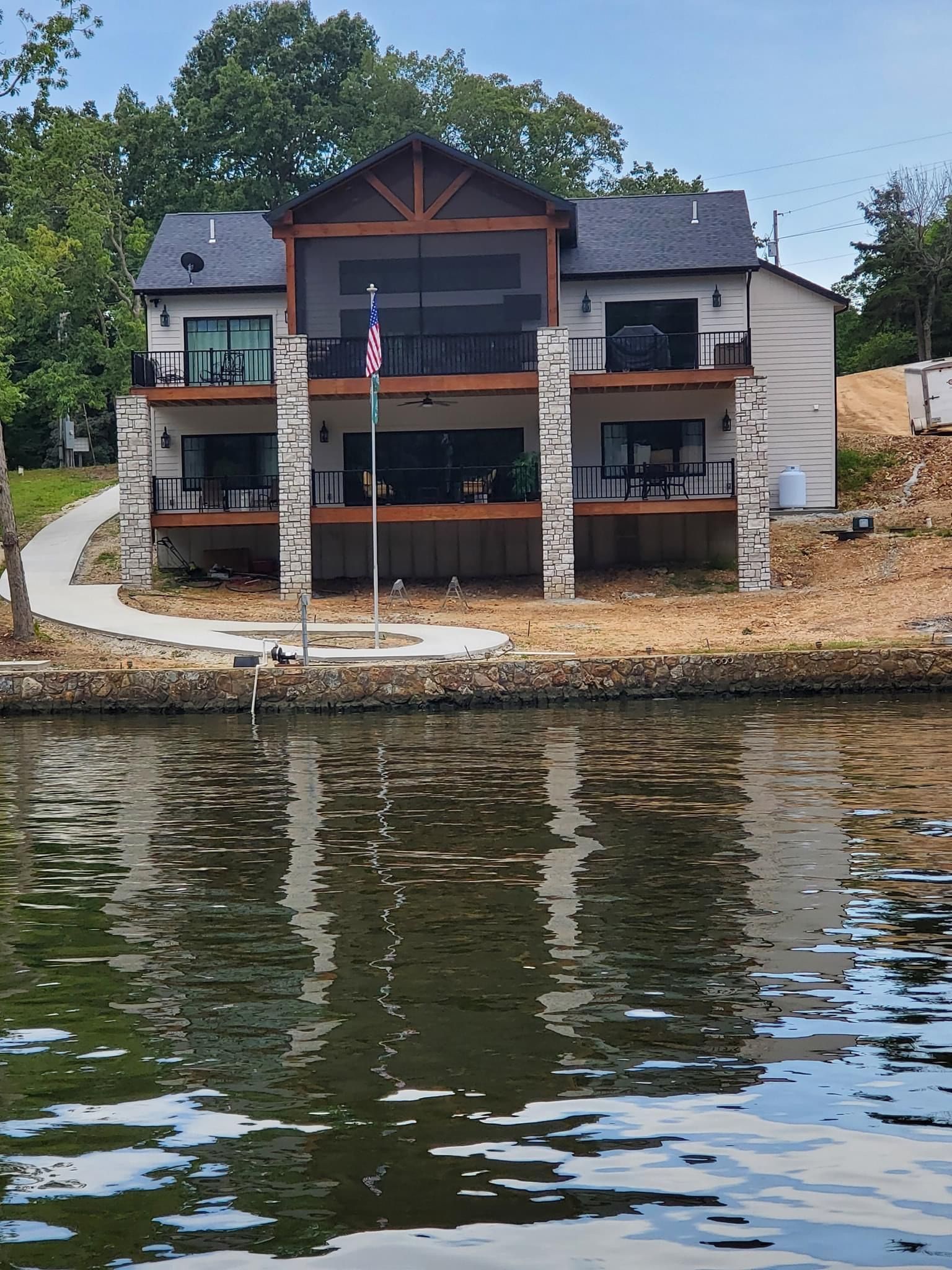 Lakeside house with balconies and an American flag, reflected in calm water.