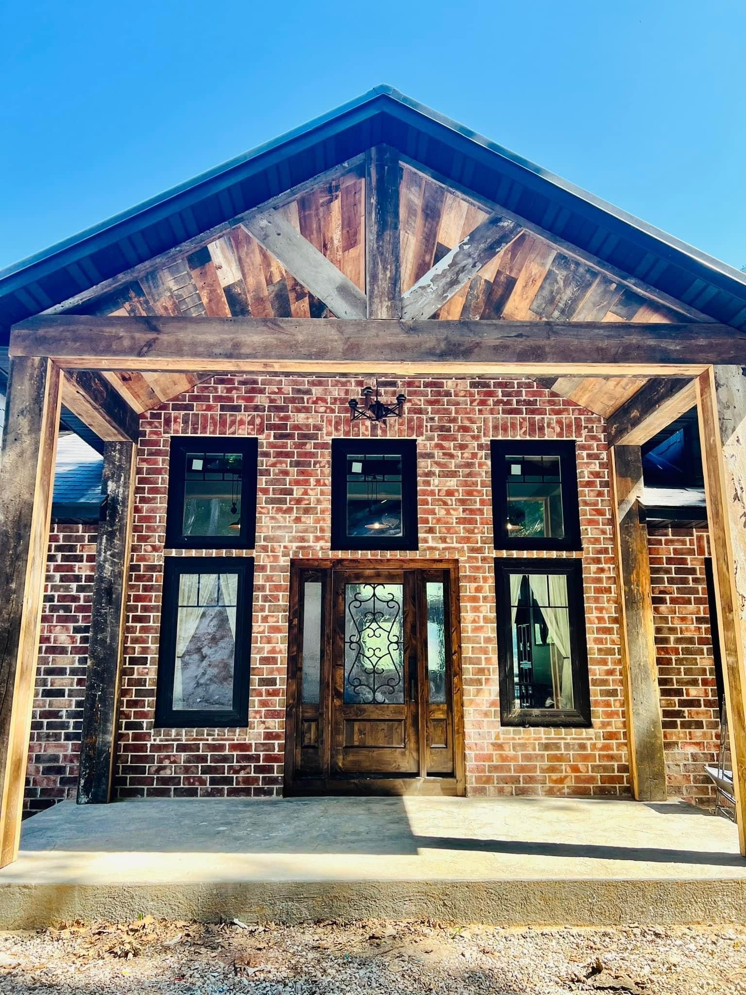 Rustic brick storefront with wooden beams, large windows, and a peaked roof in daylight