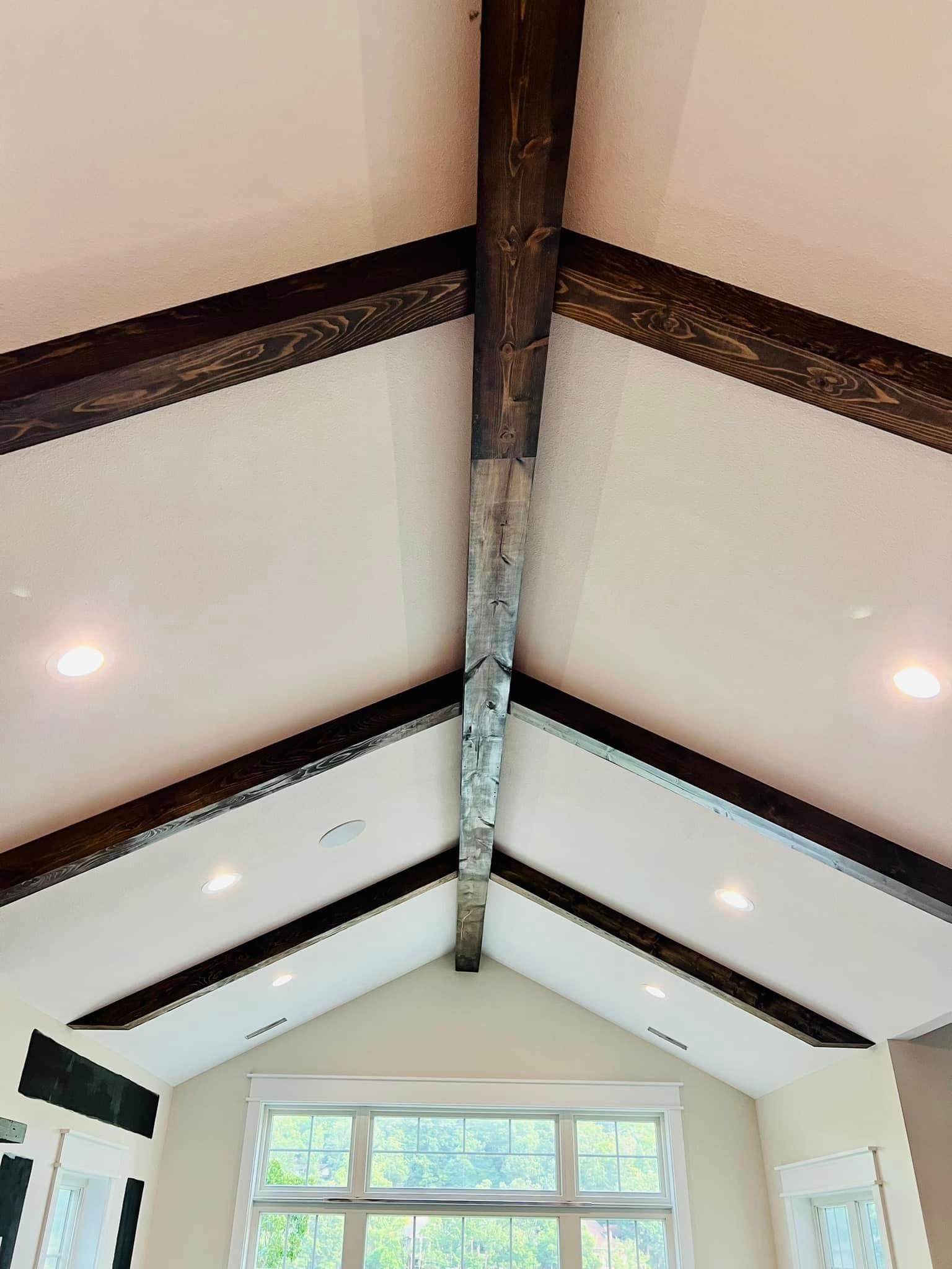 Vaulted ceiling with exposed dark beams and recessed lights above a large window.