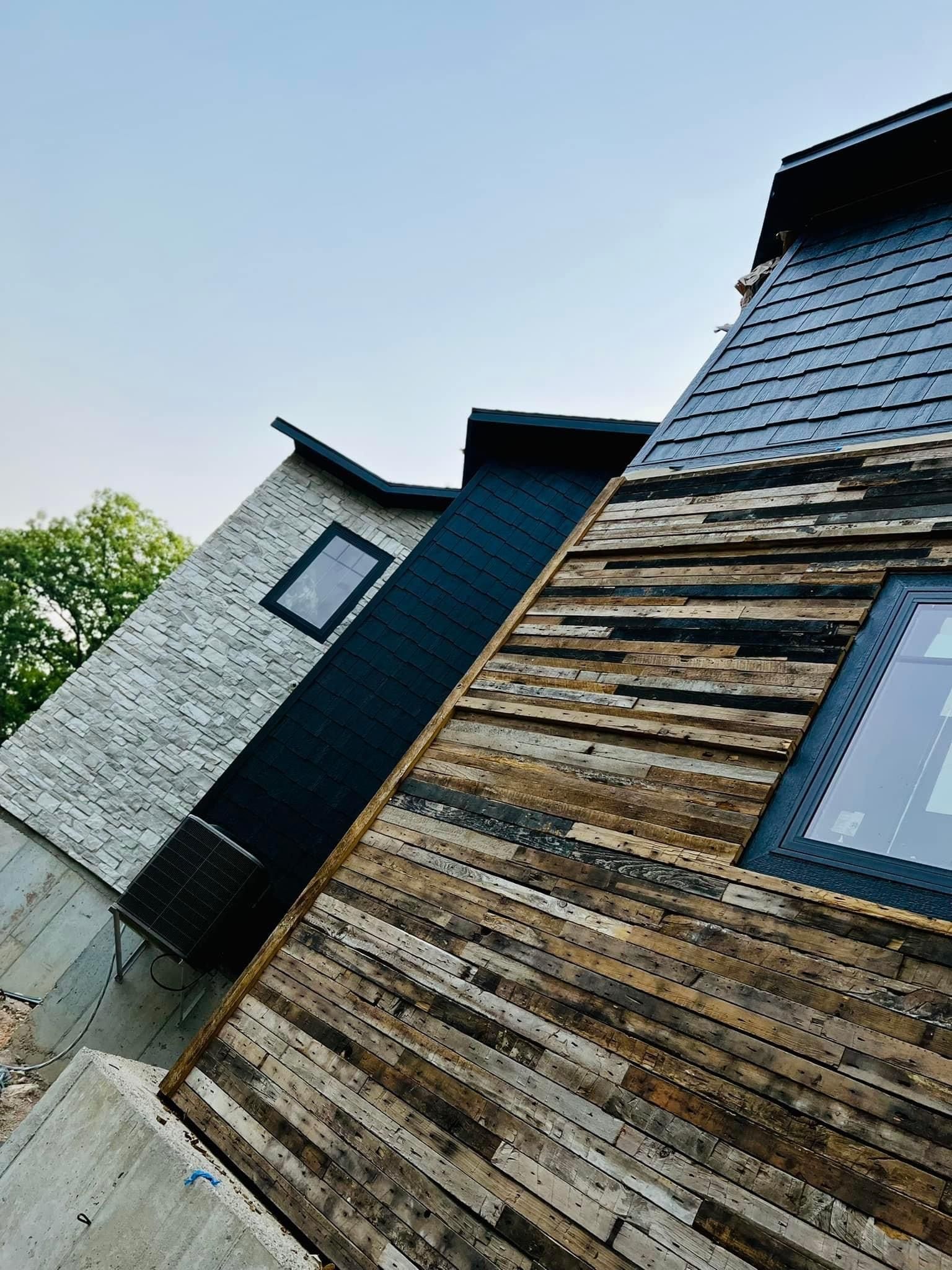 Tilted view of modern houses with wooden siding, gray roof tiles, and a small window under a pale sky