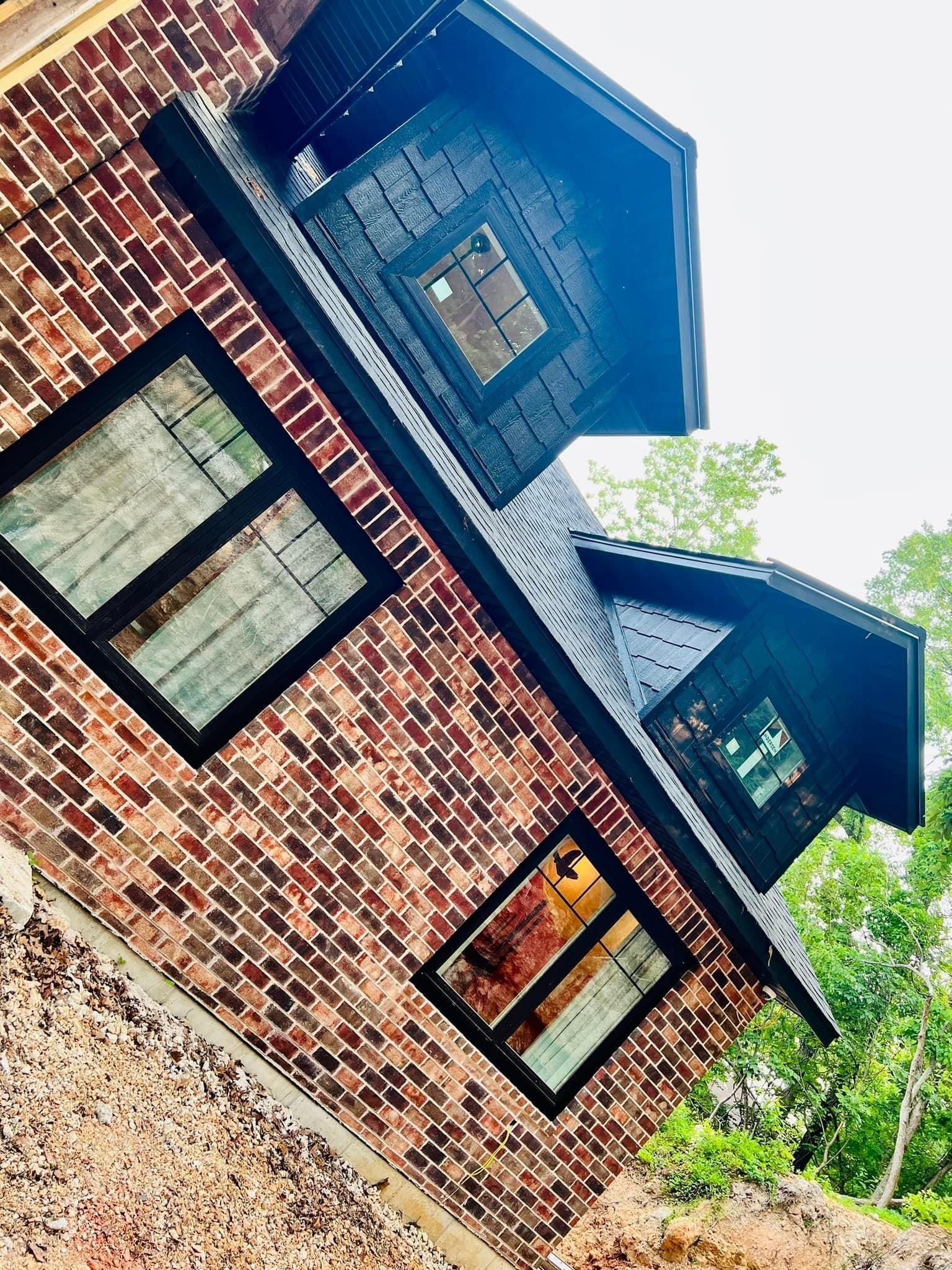 Brick house with blue roof and black-trimmed windows, viewed at a tilted angle with trees nearby