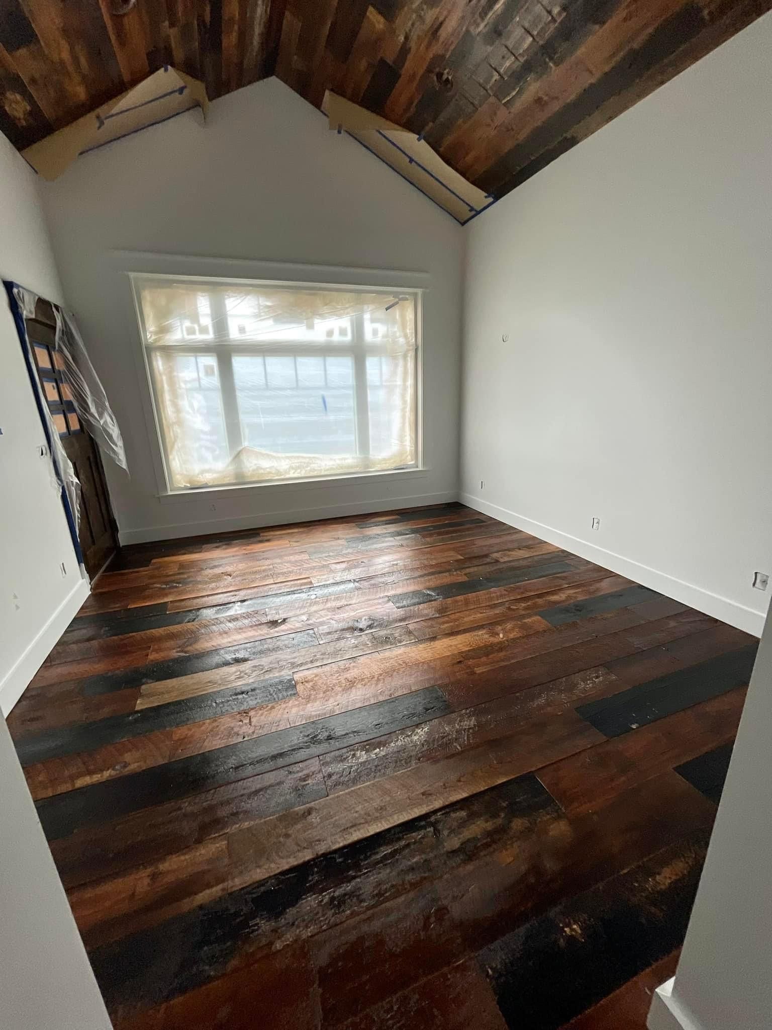 Empty room with slanted wood ceiling, dark hardwood floor, and a window on the far wall.