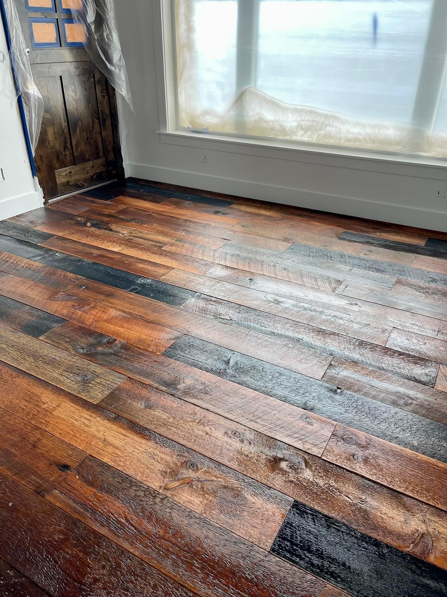 Wooden floorboards by a window, with warm and dark stained planks and sunlight reflections.