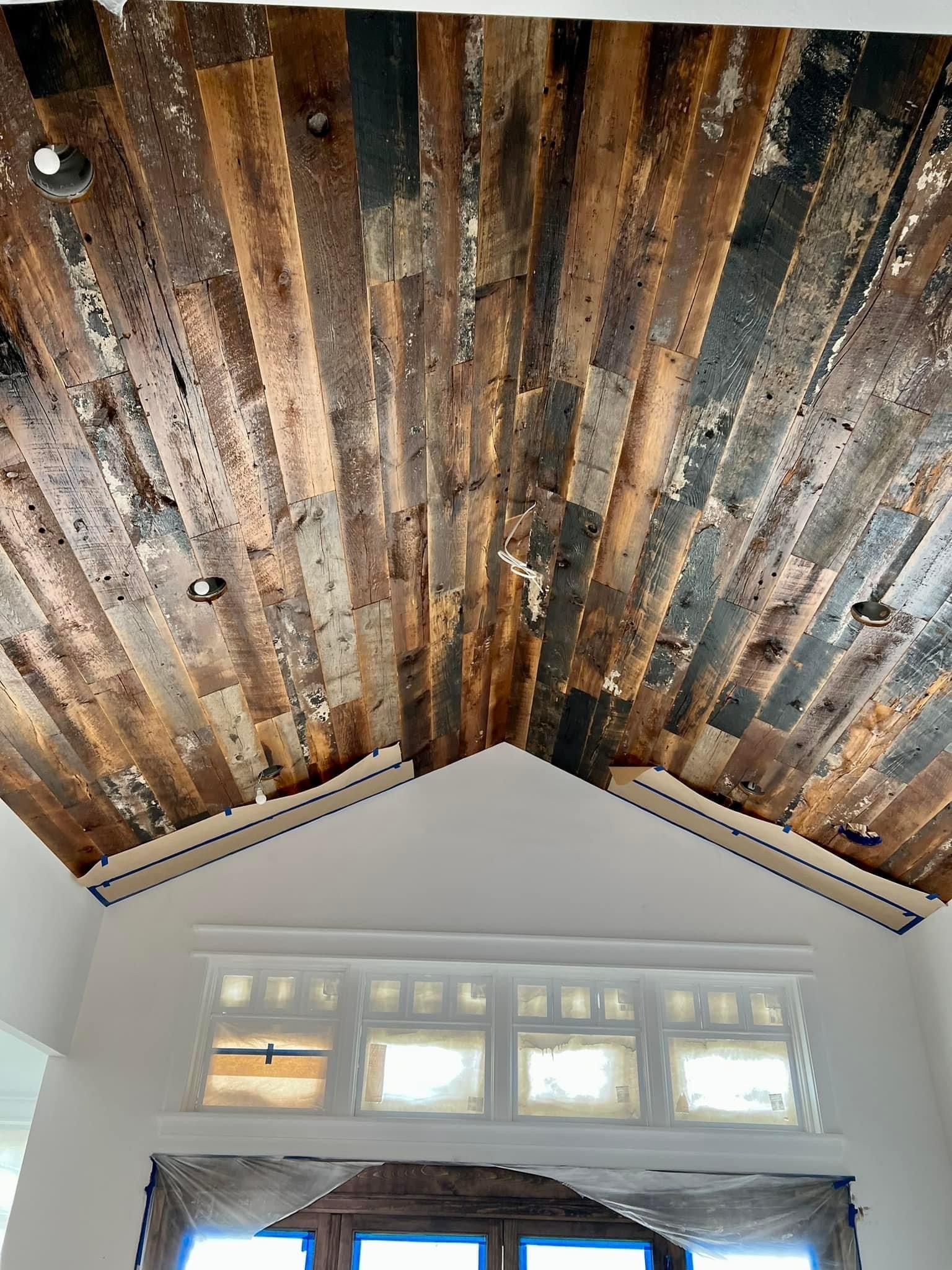 Rustic wood-plank vaulted ceiling above a windowed wall in a bright room