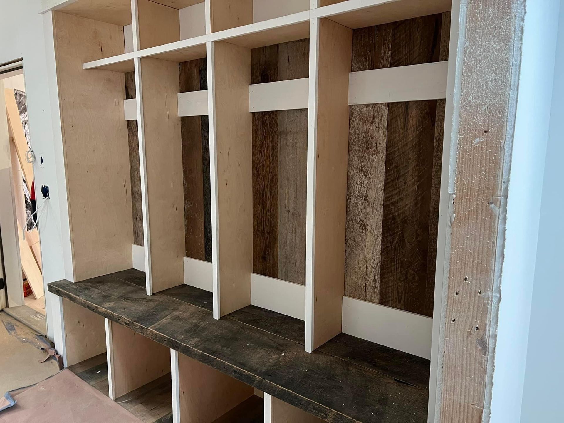 Built-in wooden cubby shelves with vertical dividers and a dark base bench in a hallway