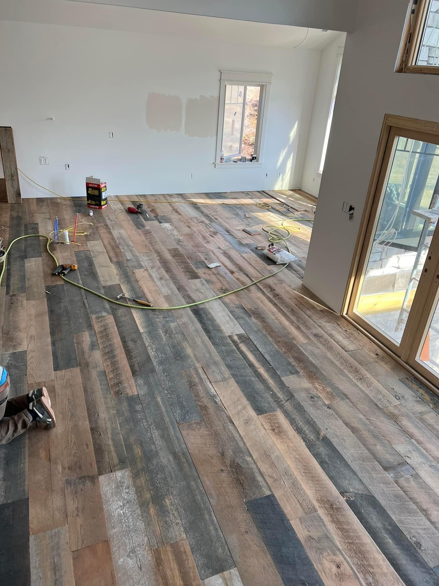 Empty room under renovation with multicolored wood-look flooring and scattered tools near windows.