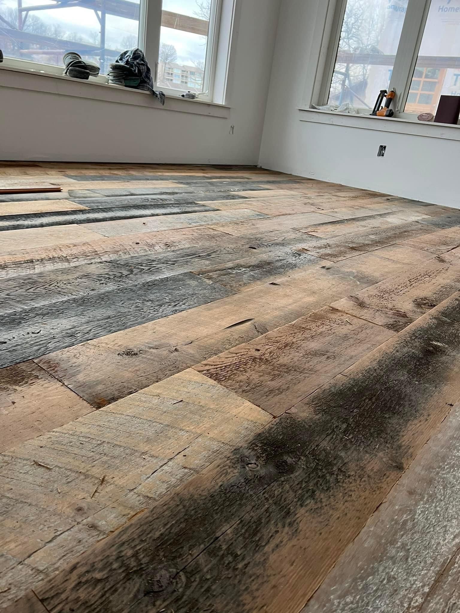 Empty room with unfinished wood plank floor and large windows letting in daylight