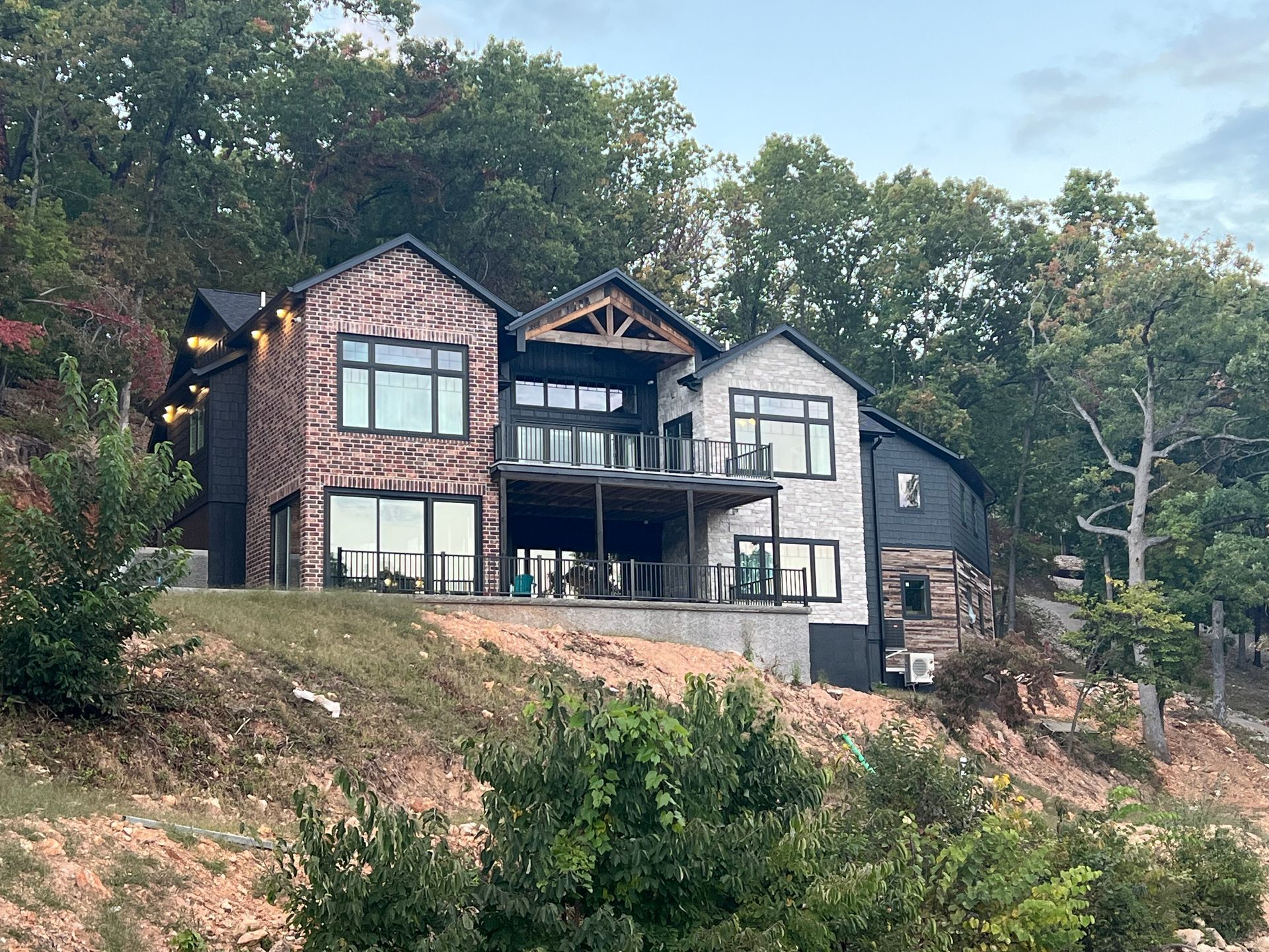 Modern hillside house with black-and-white trim and brick facade surrounded by trees