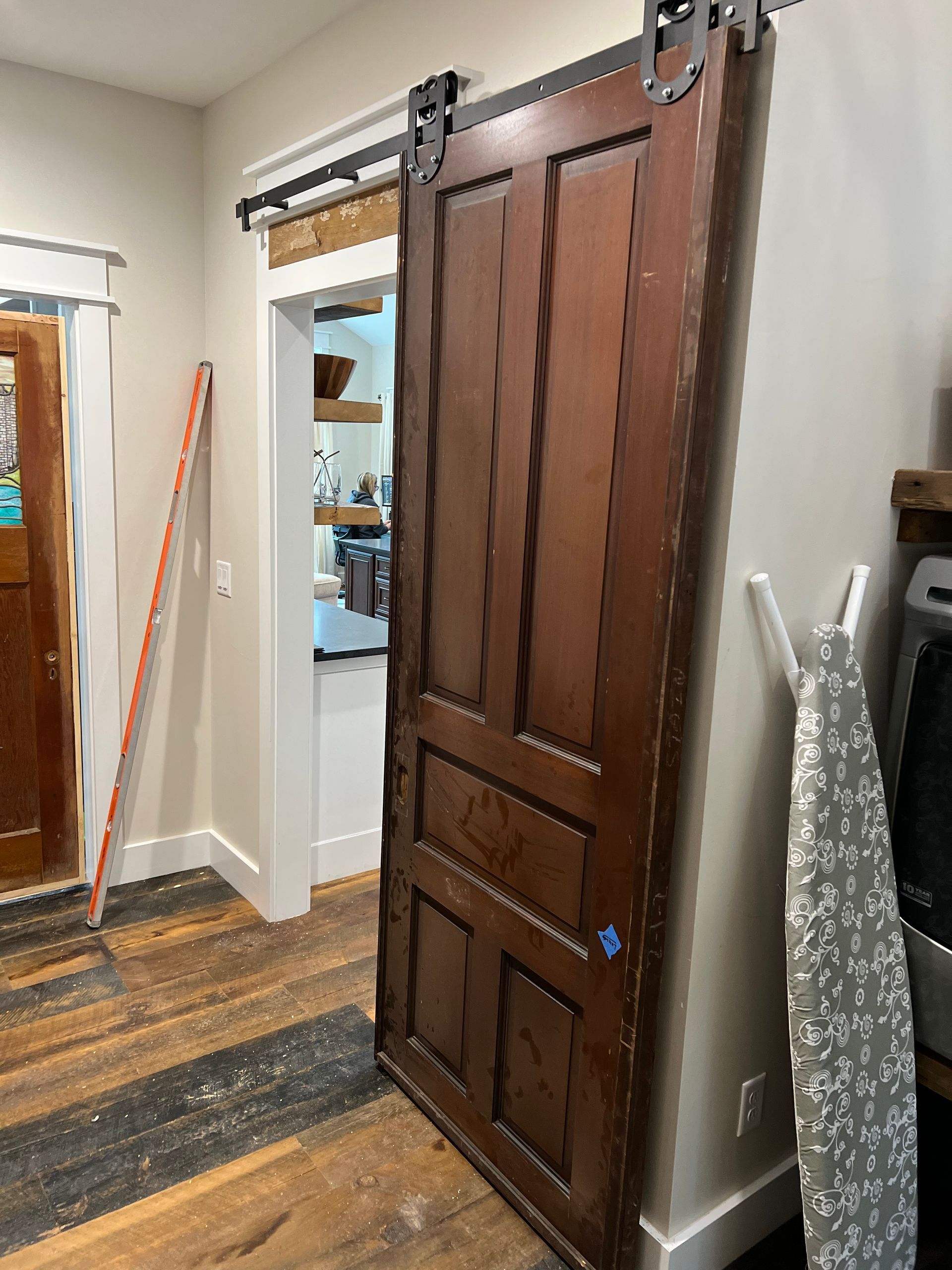 Dark wooden sliding barn door in a home hallway with exposed hardware and patterned floorboards