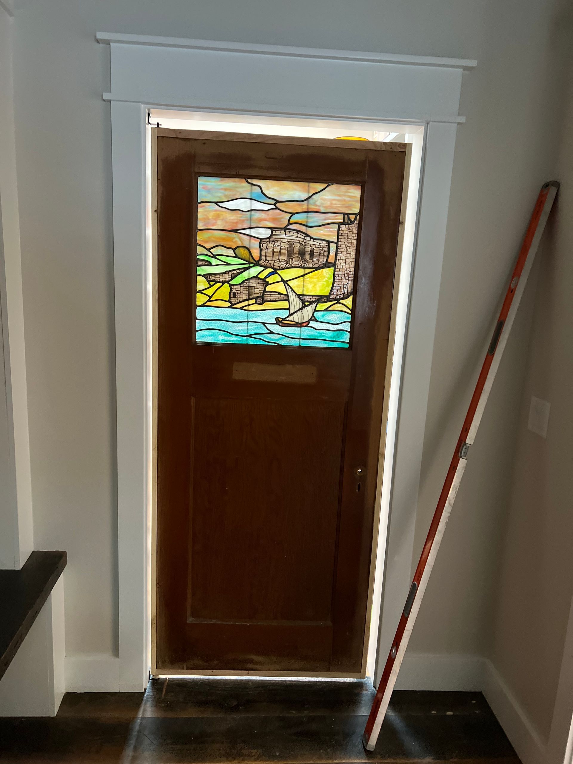 Wooden door with stained glass panel in a narrow hallway, with a striped pole leaning beside it.