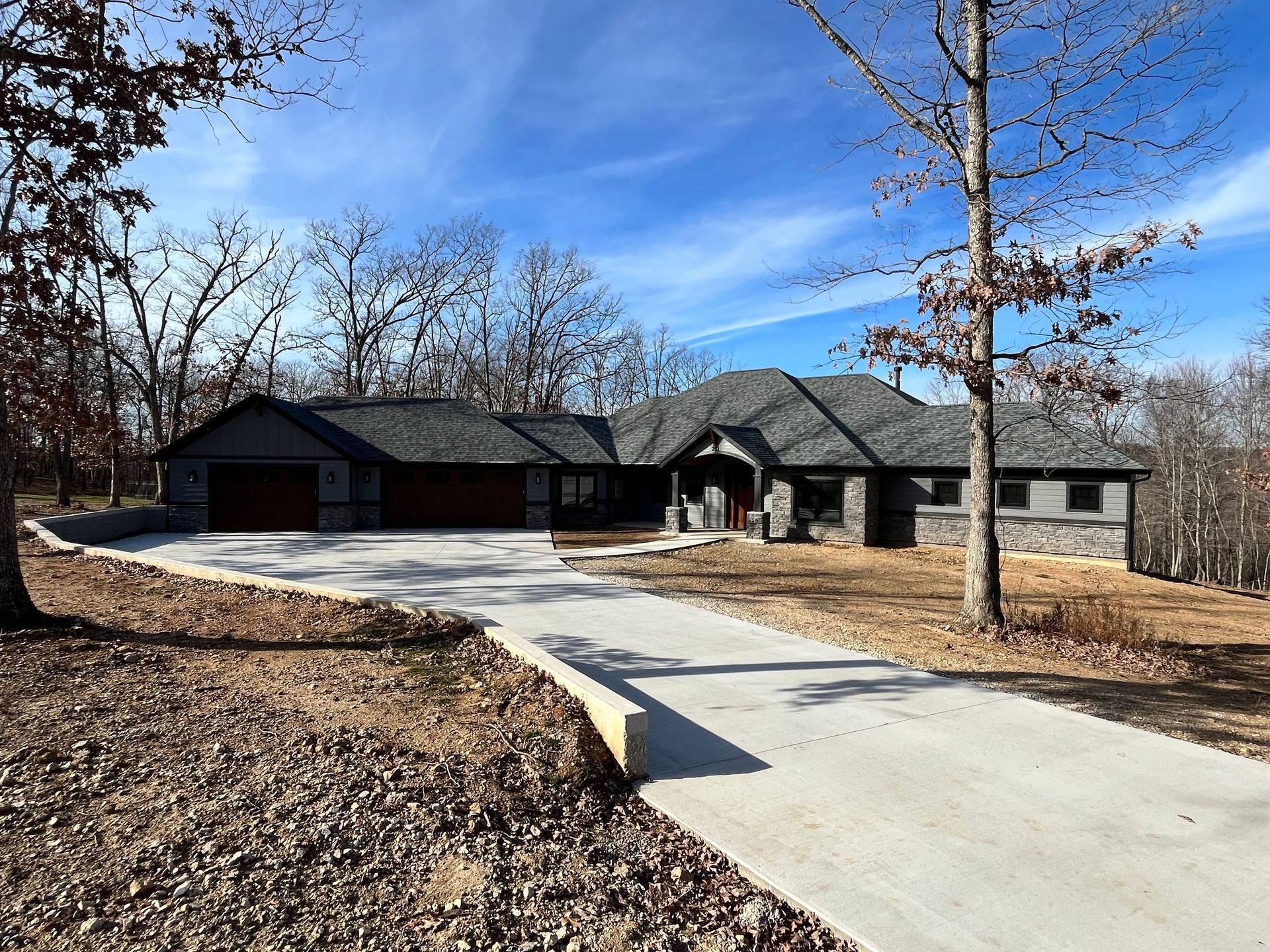 Single-story modern house with a curved driveway, stone facade, and bare trees under a blue sky.
