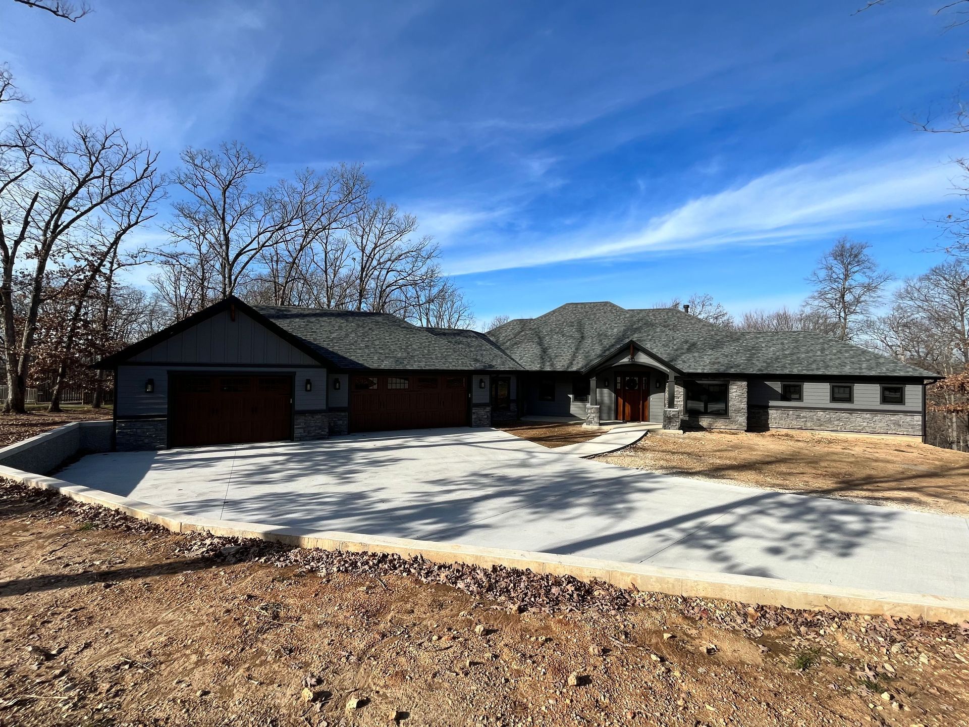 Single-story brick house with a curved driveway, leafless trees, and blue sky in a rural setting
