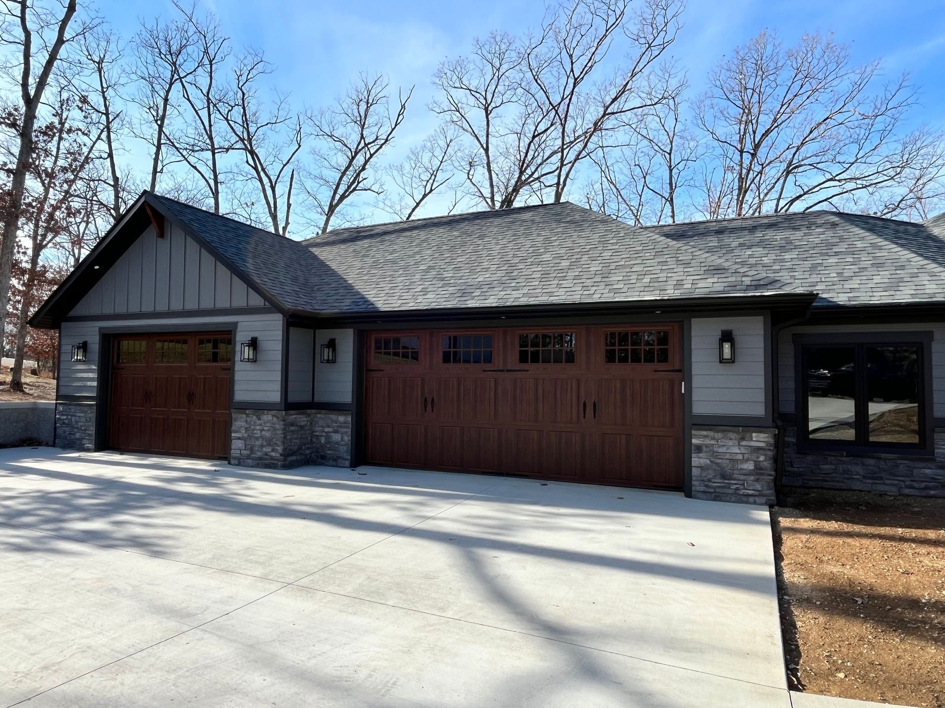 Single-story house with stone and wood exterior, two garage doors, and leafless trees in front