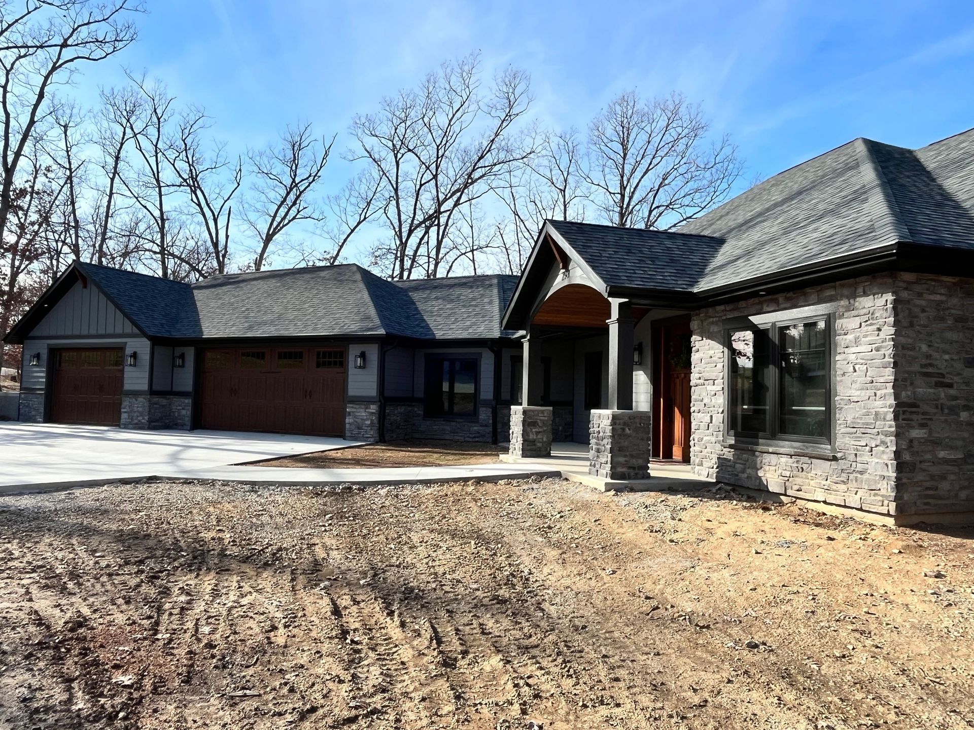 Suburban stone house with three-car garage and bare trees on a sunny day