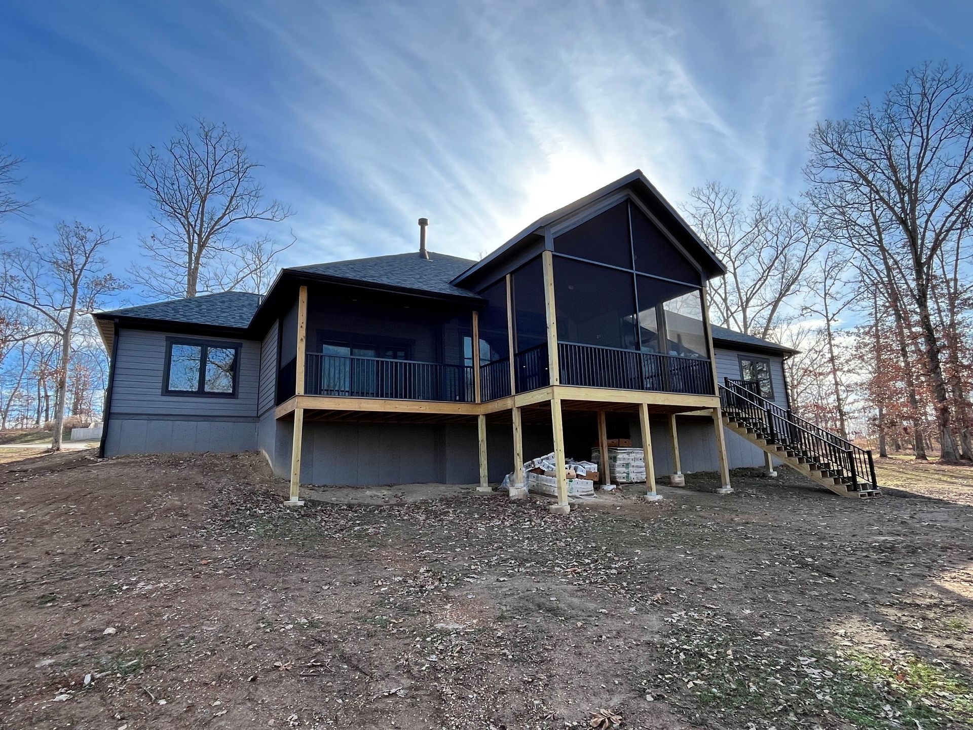 Rustic cabin on a hillside under a bright blue sky, with a covered porch and bare trees nearby