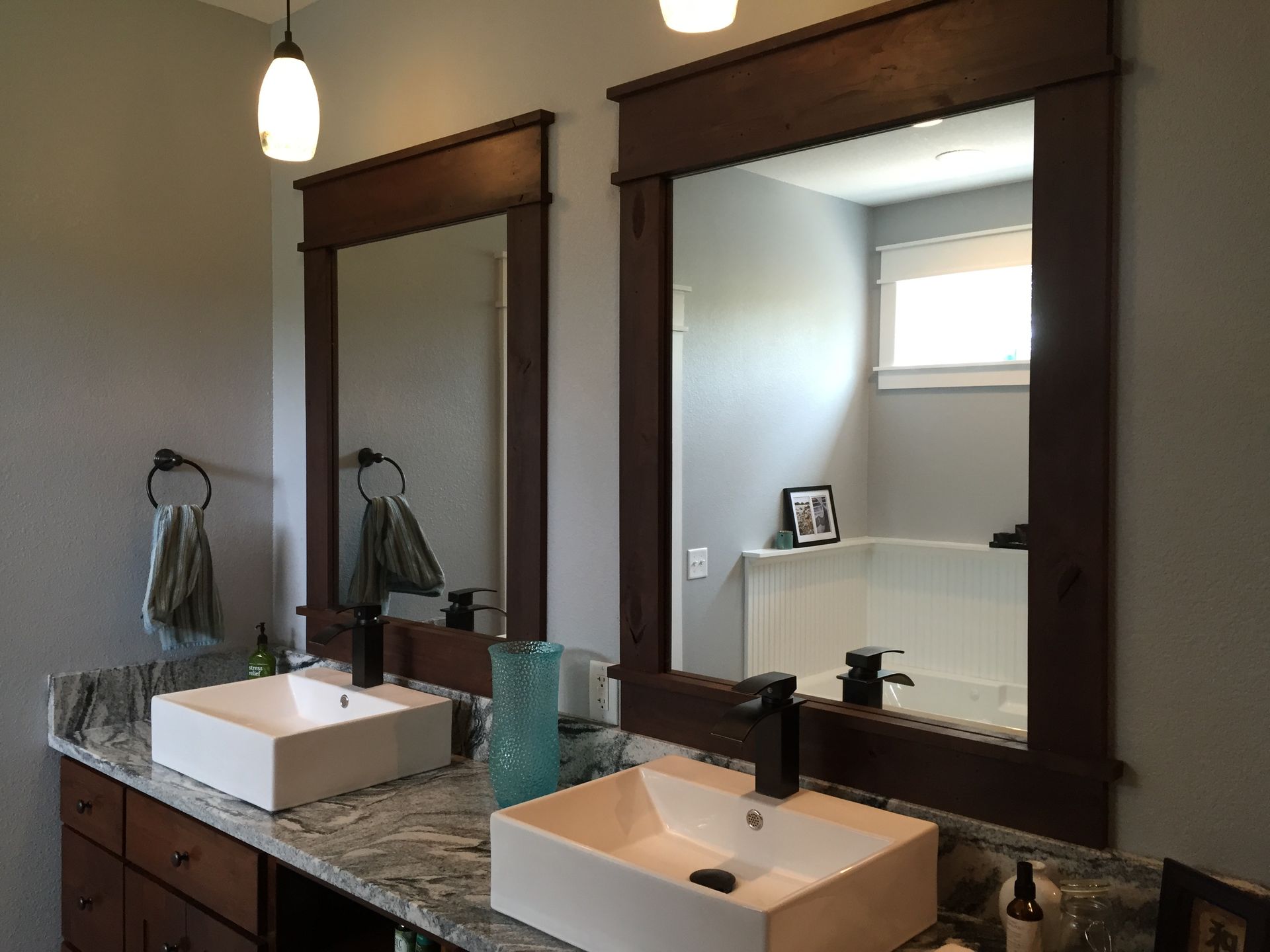 Bathroom vanity with two sinks, large mirrors, and granite countertop under a hanging light.