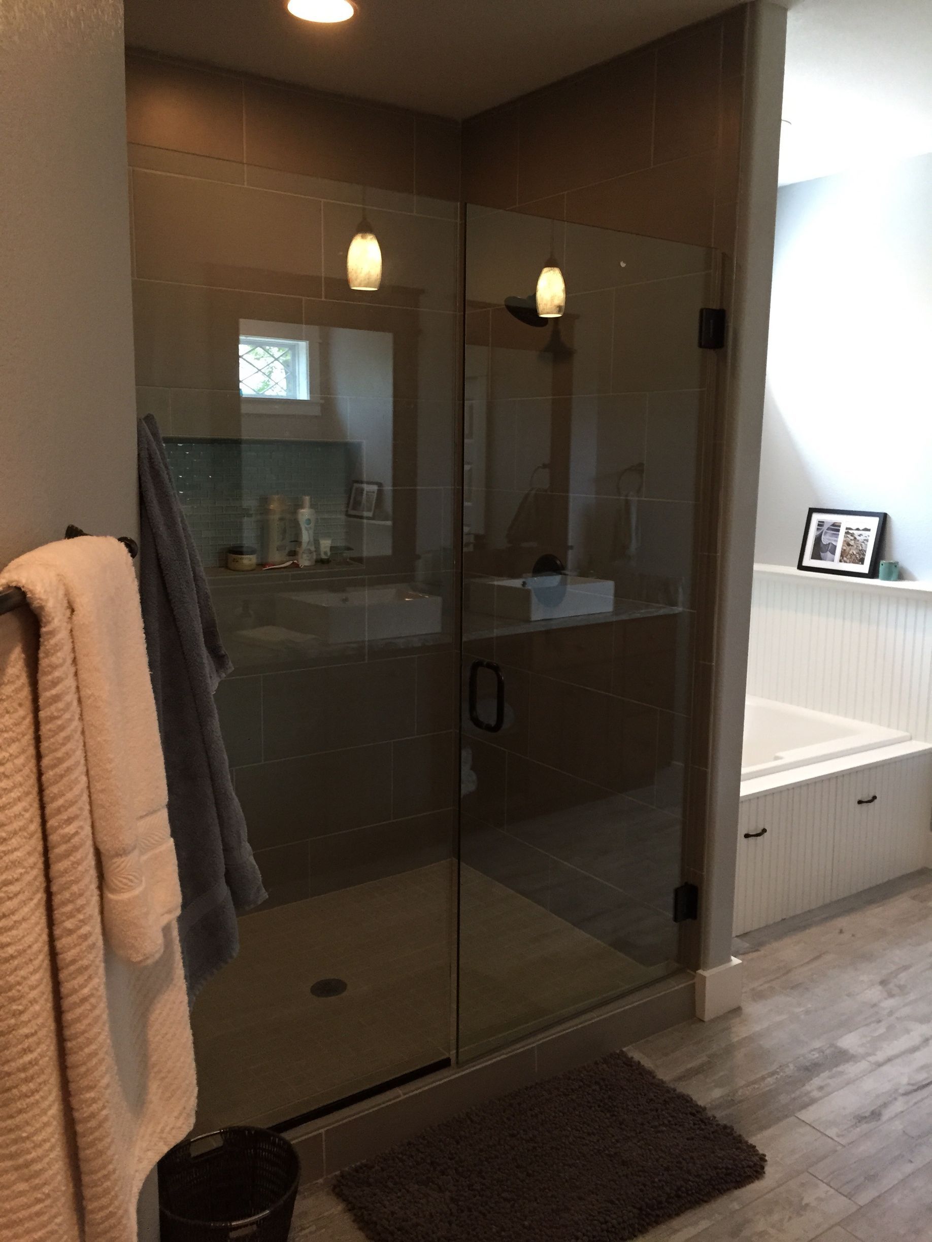Modern bathroom with glass shower enclosure, towel, and bath mat under warm lighting