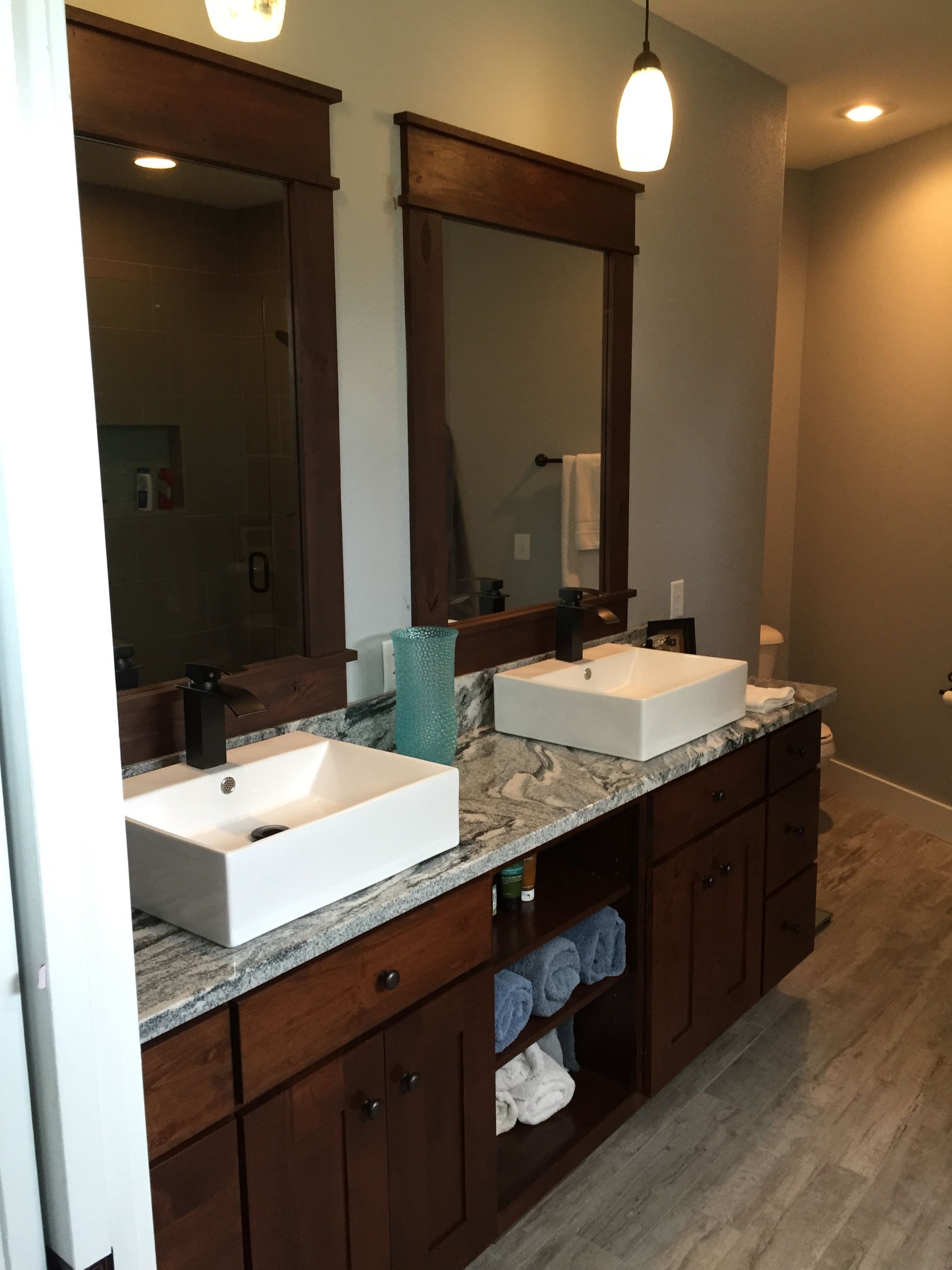Bathroom vanity with two sinks, granite countertop, and large mirrors in a modern tiled room