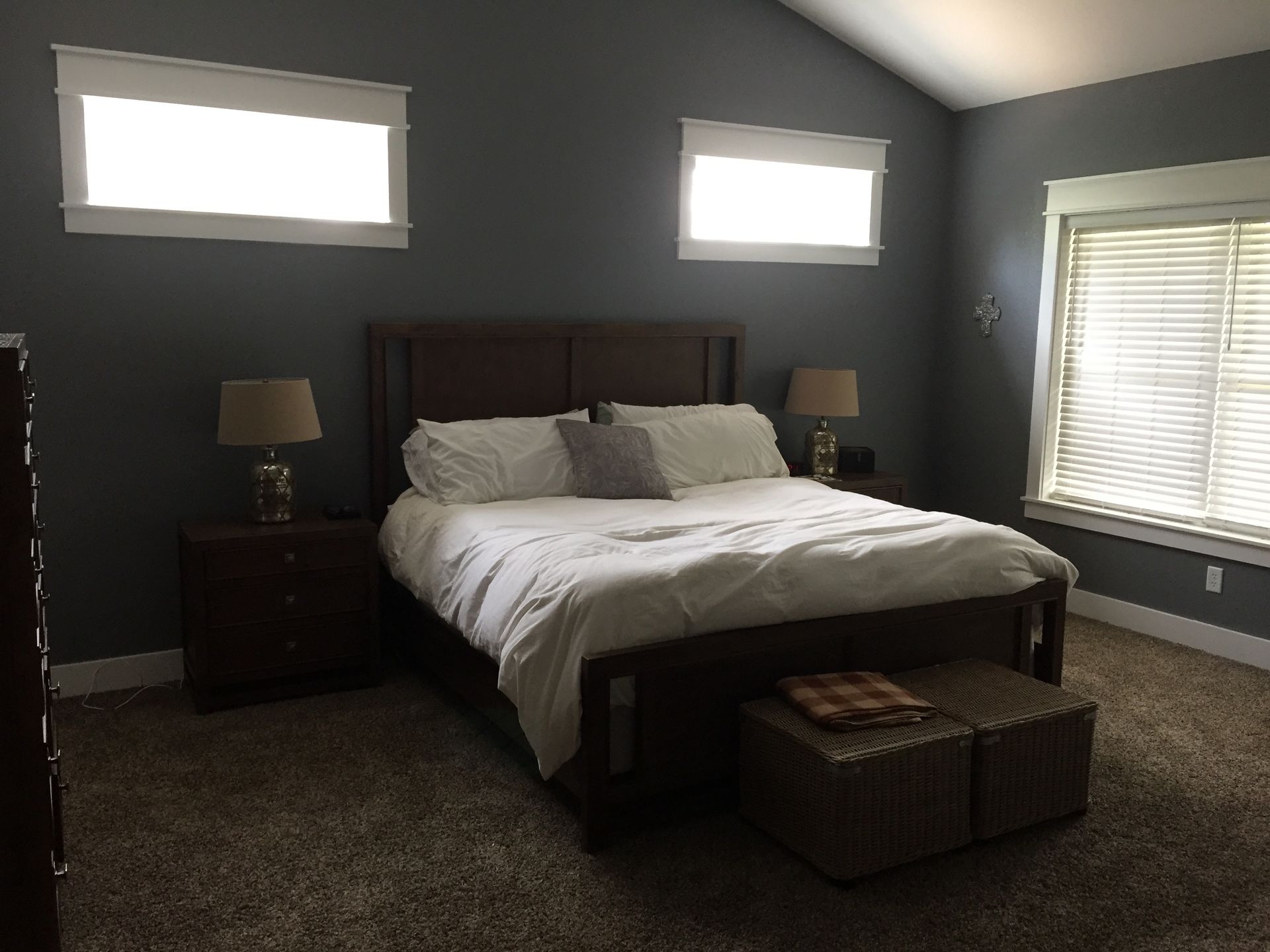 Bedroom with a large bed, dark walls, bedside lamps, and two small windows with blinds.