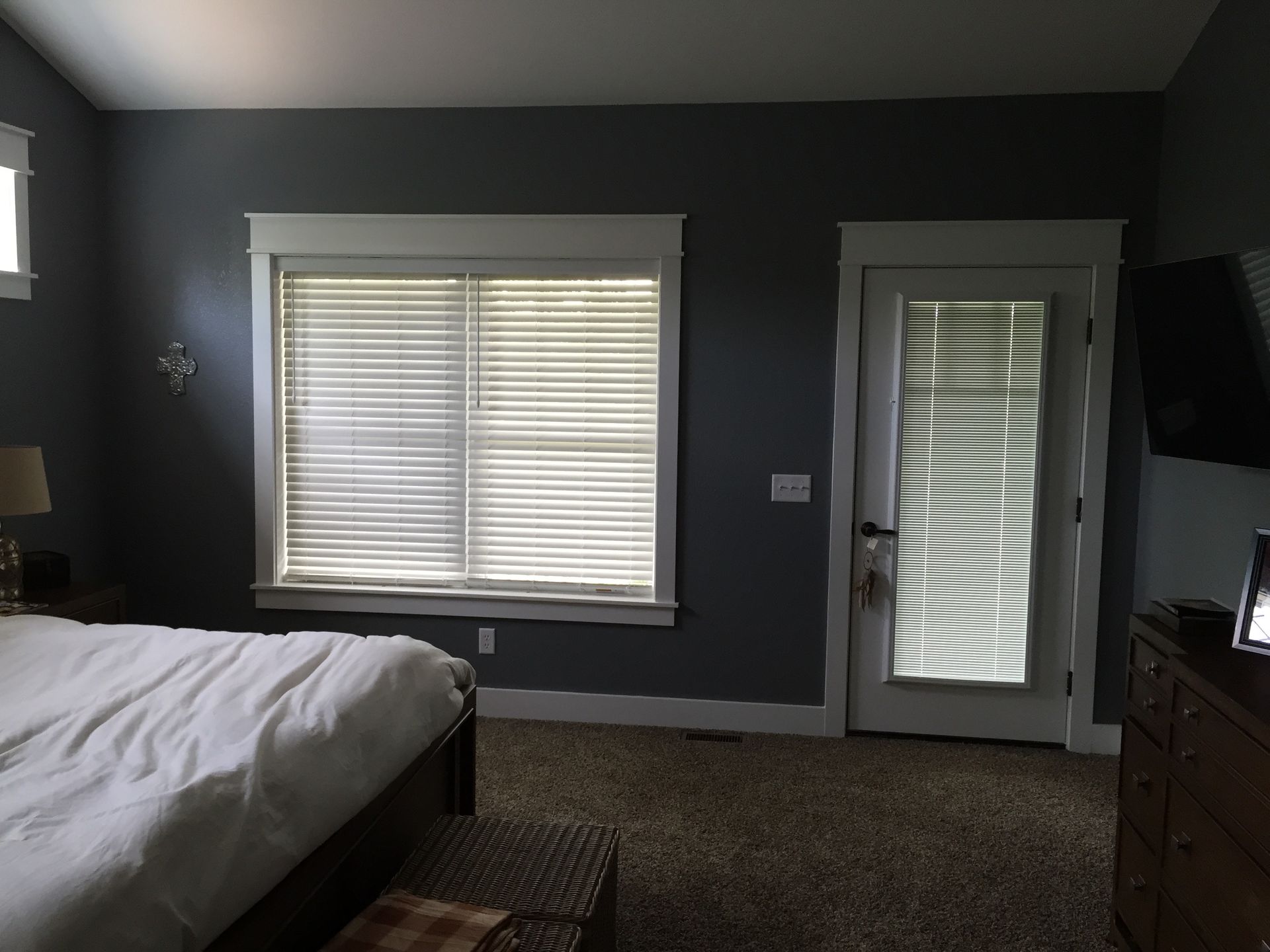 Bedroom with dark gray walls, white bed, window blinds, and a glass door with blinds.