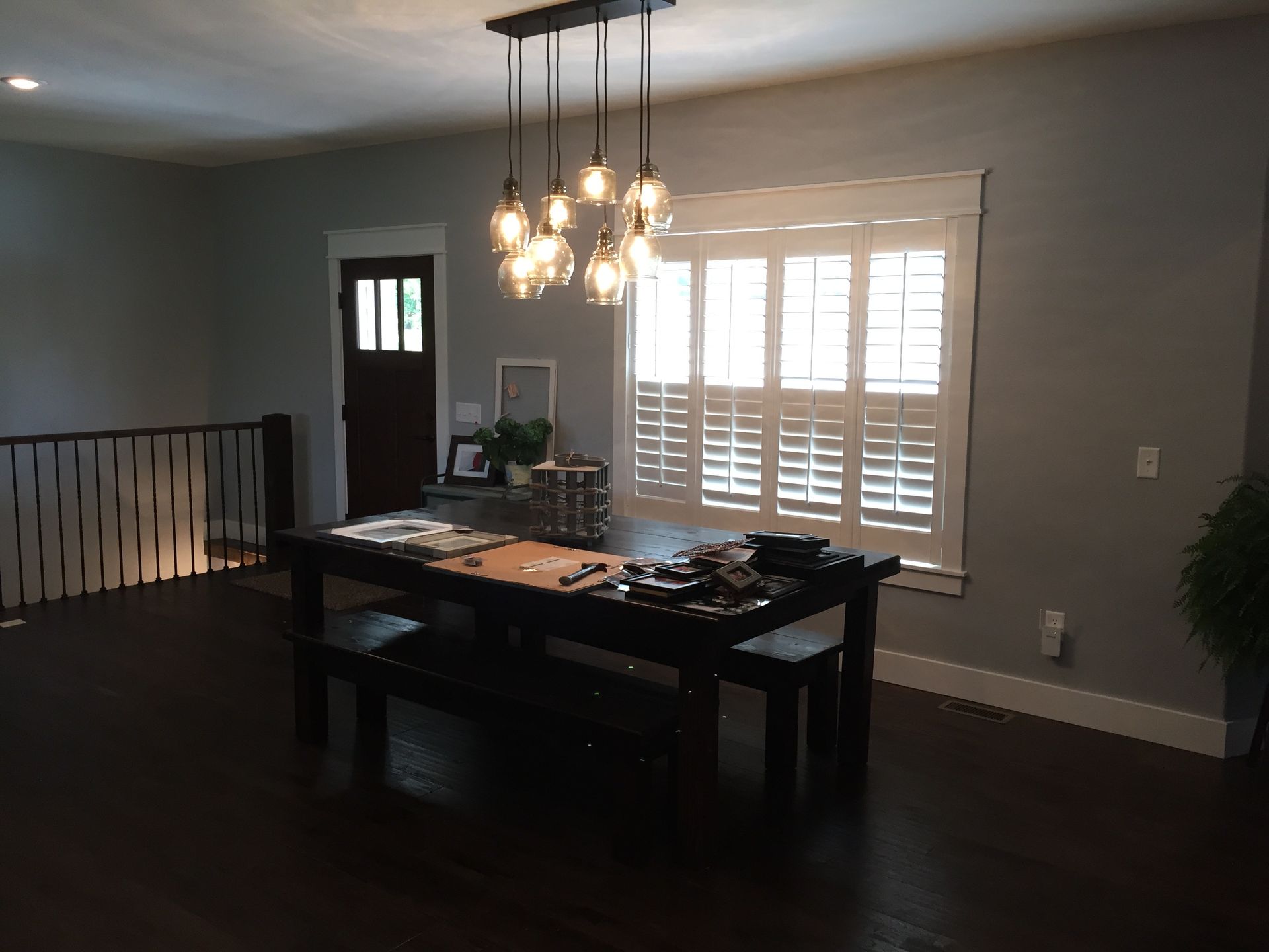 Dining room with a dark table, hanging light fixture, and sunlit window blinds on gray walls