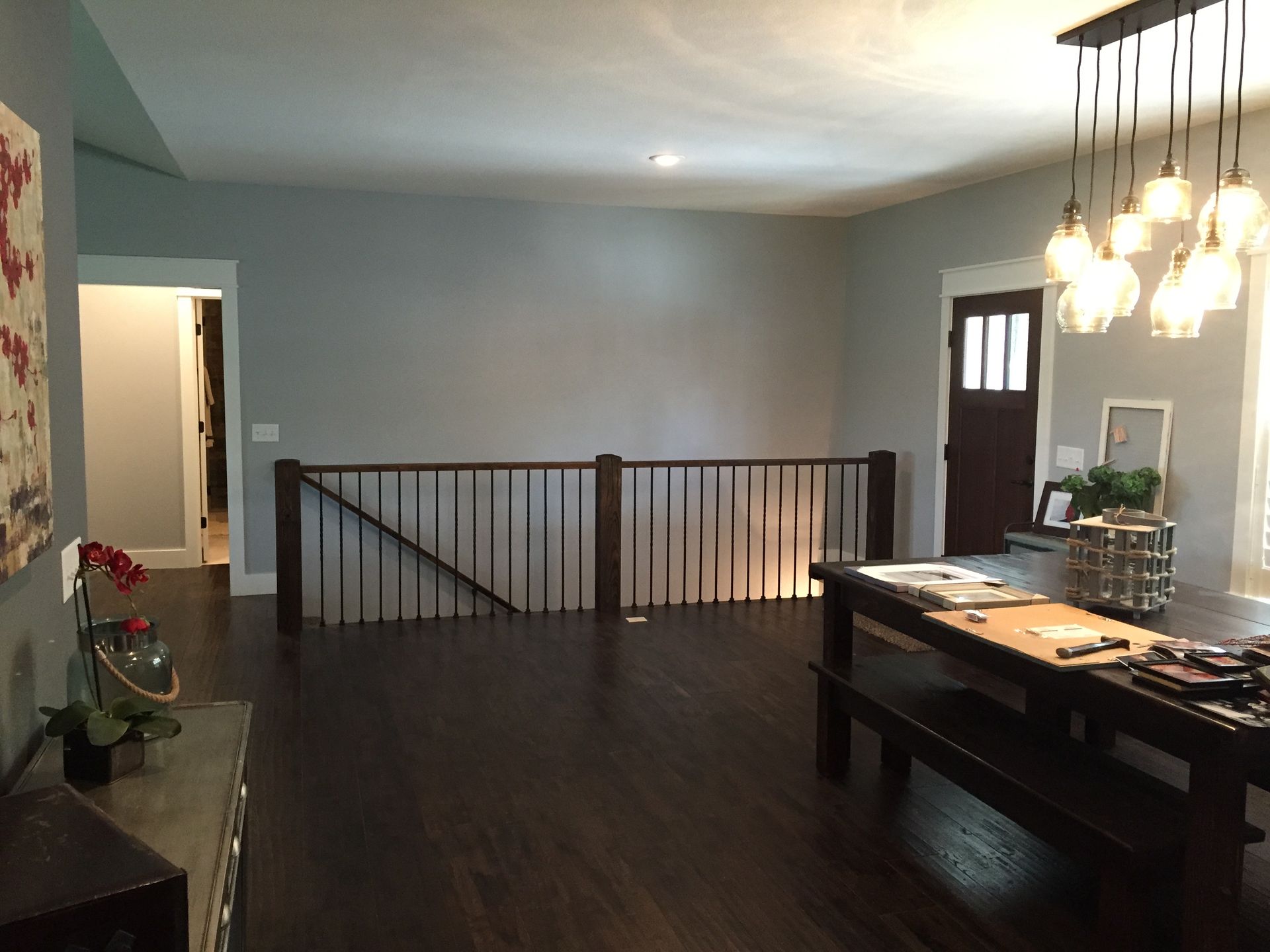Modern open dining room with dark wood floor, gray walls, railing, pendant lights, and a table by the front door