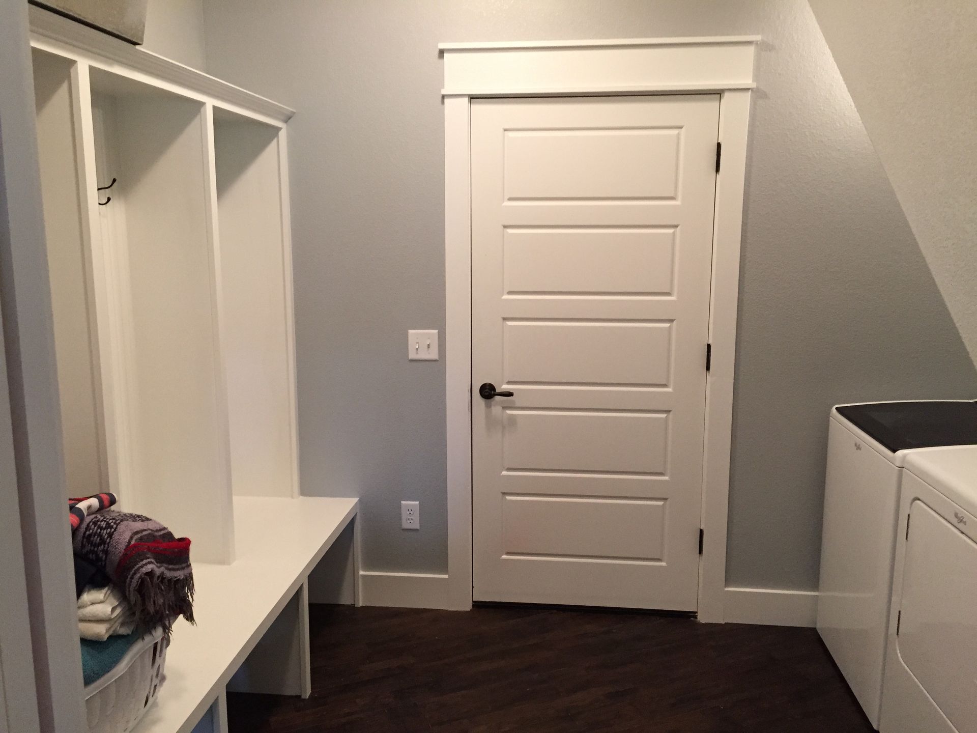 Small white mudroom with bench cubbies, built-in cabinets, and a closed door.