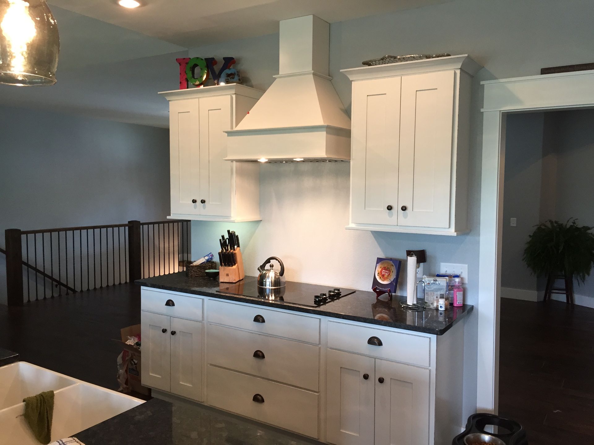Kitchen with white cabinets, stove hood, island, and dark railing in an open living space