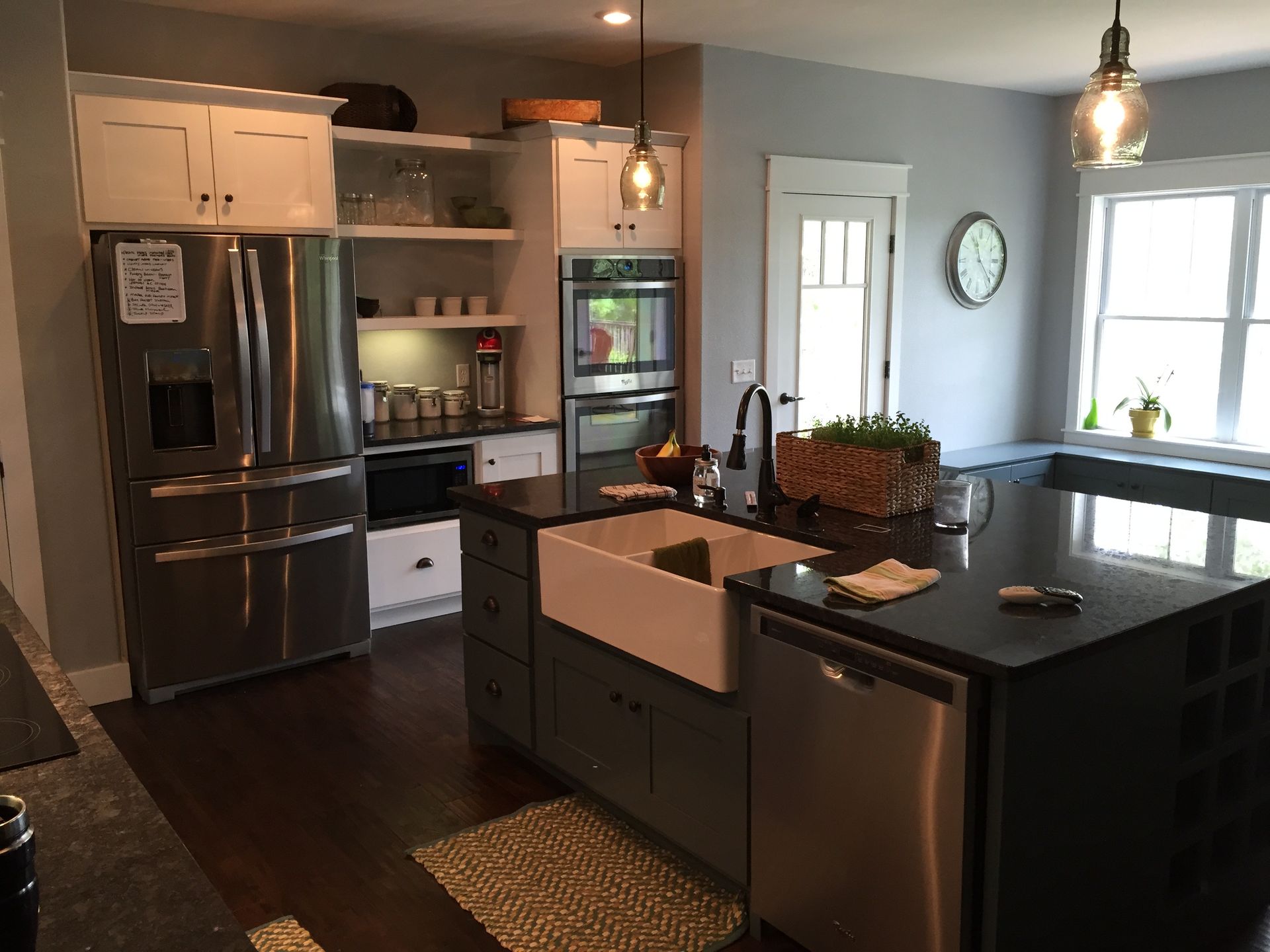 Modern kitchen with stainless steel appliances, dark island, pendant lights, and a bright windowed dining area