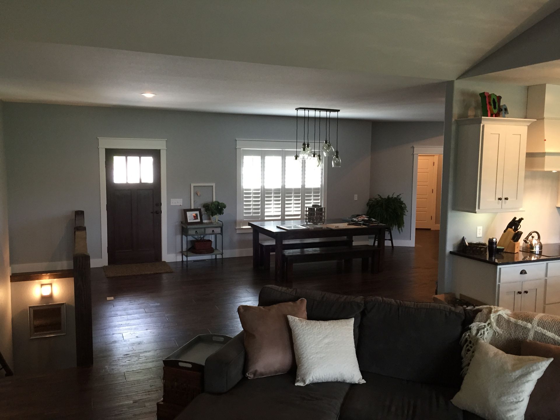 Cozy living room with dark sofa, dining table, tiled floor, and kitchen area in the background