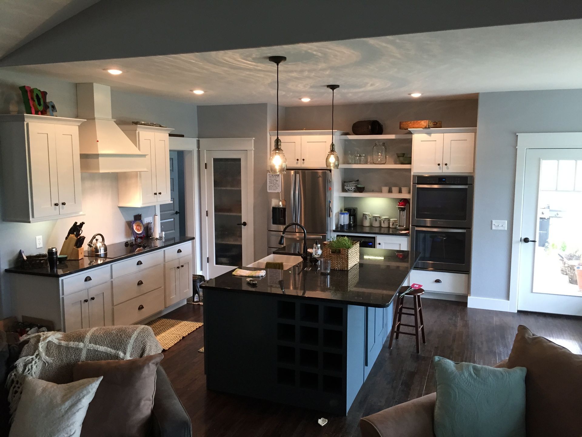 Bright modern kitchen with white cabinets, black island, pendant lights, and stools near a door.