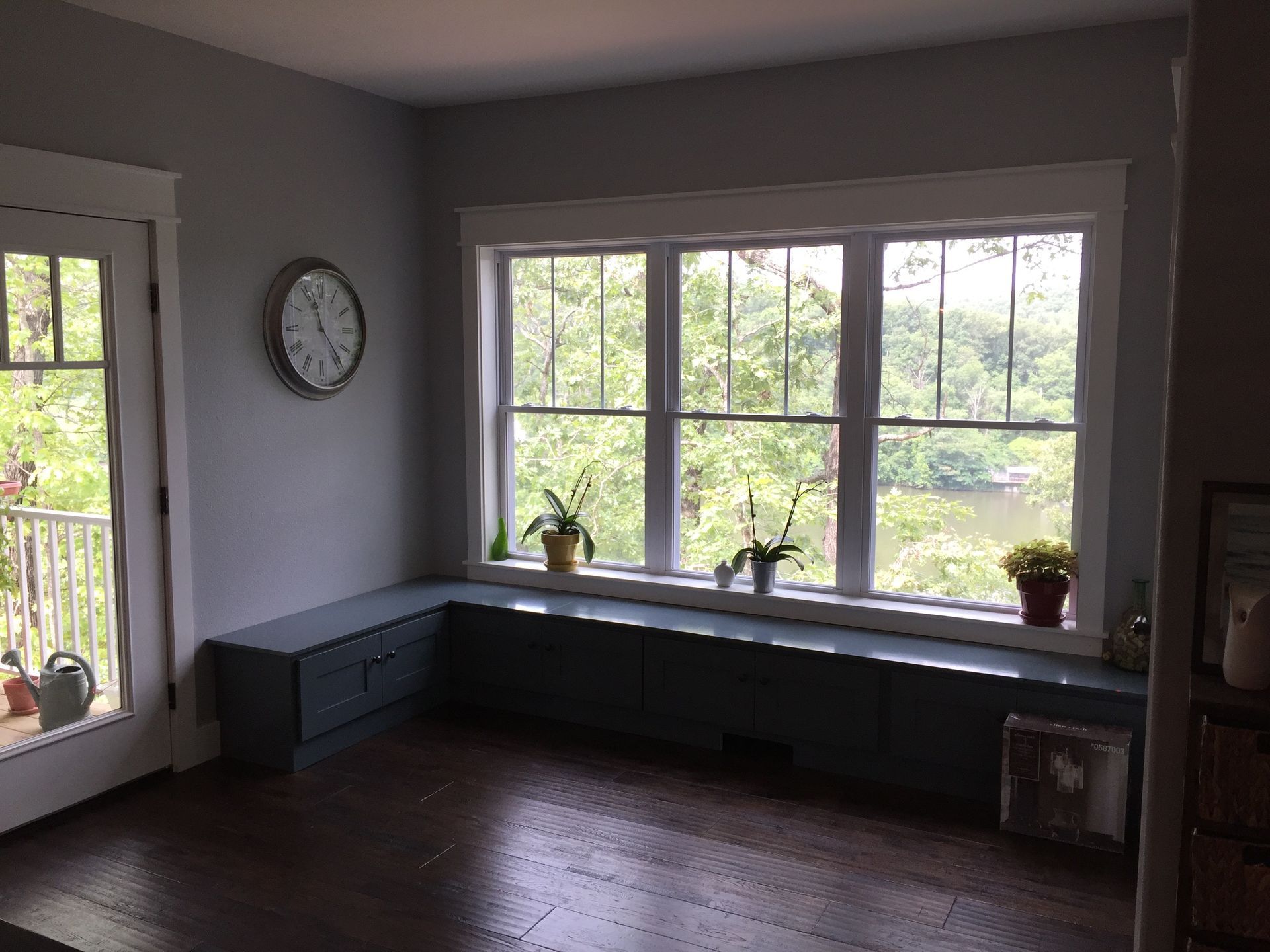 Empty living room with dark wood floors, gray walls, large windows, and a long built-in bench.