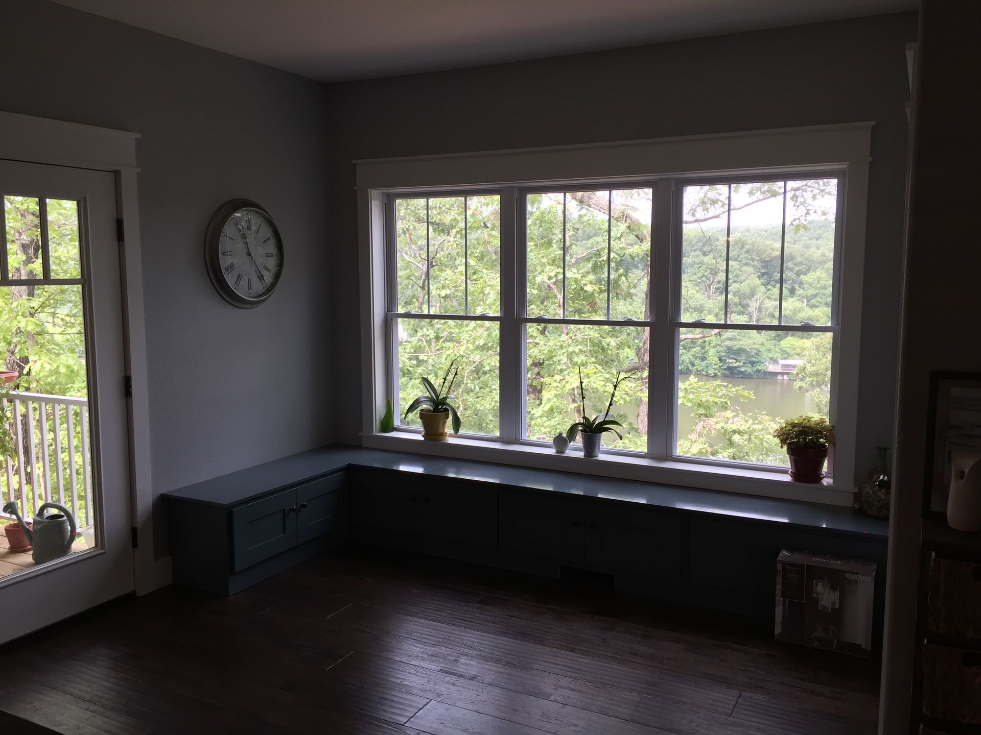 Empty room with dark wood floor, large windows, and a built-in bench under the windows.