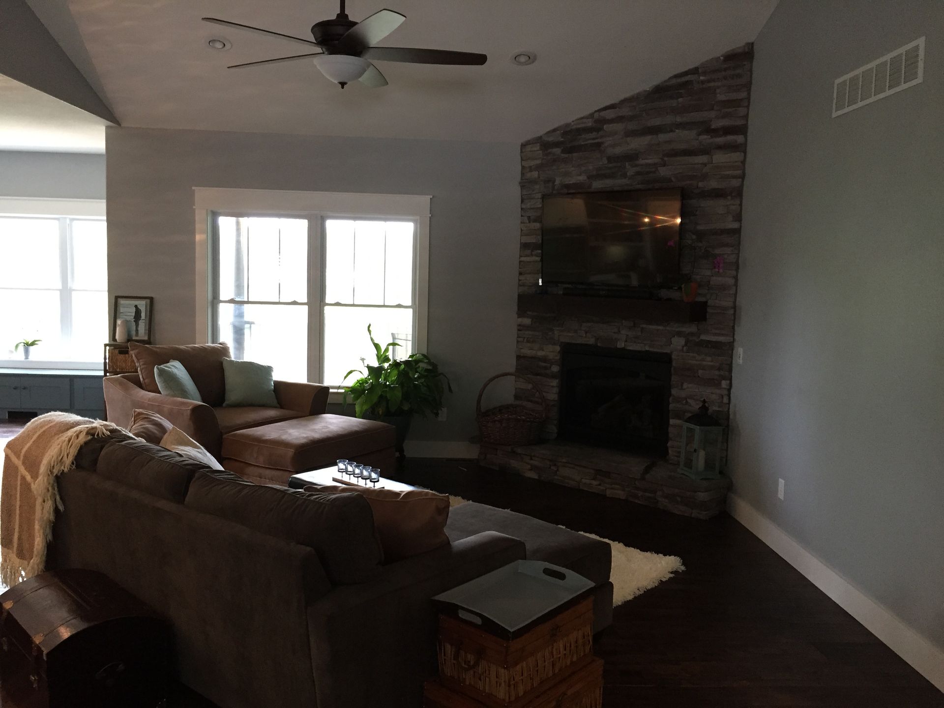 Living room with brown sectional, stone fireplace, wall-mounted TV, and large windows