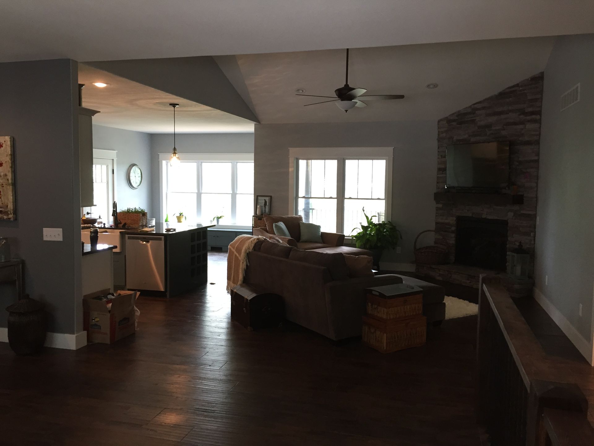 Spacious living room with dark wood floors, sofa, fireplace, and bright windows overlooking a kitchen area