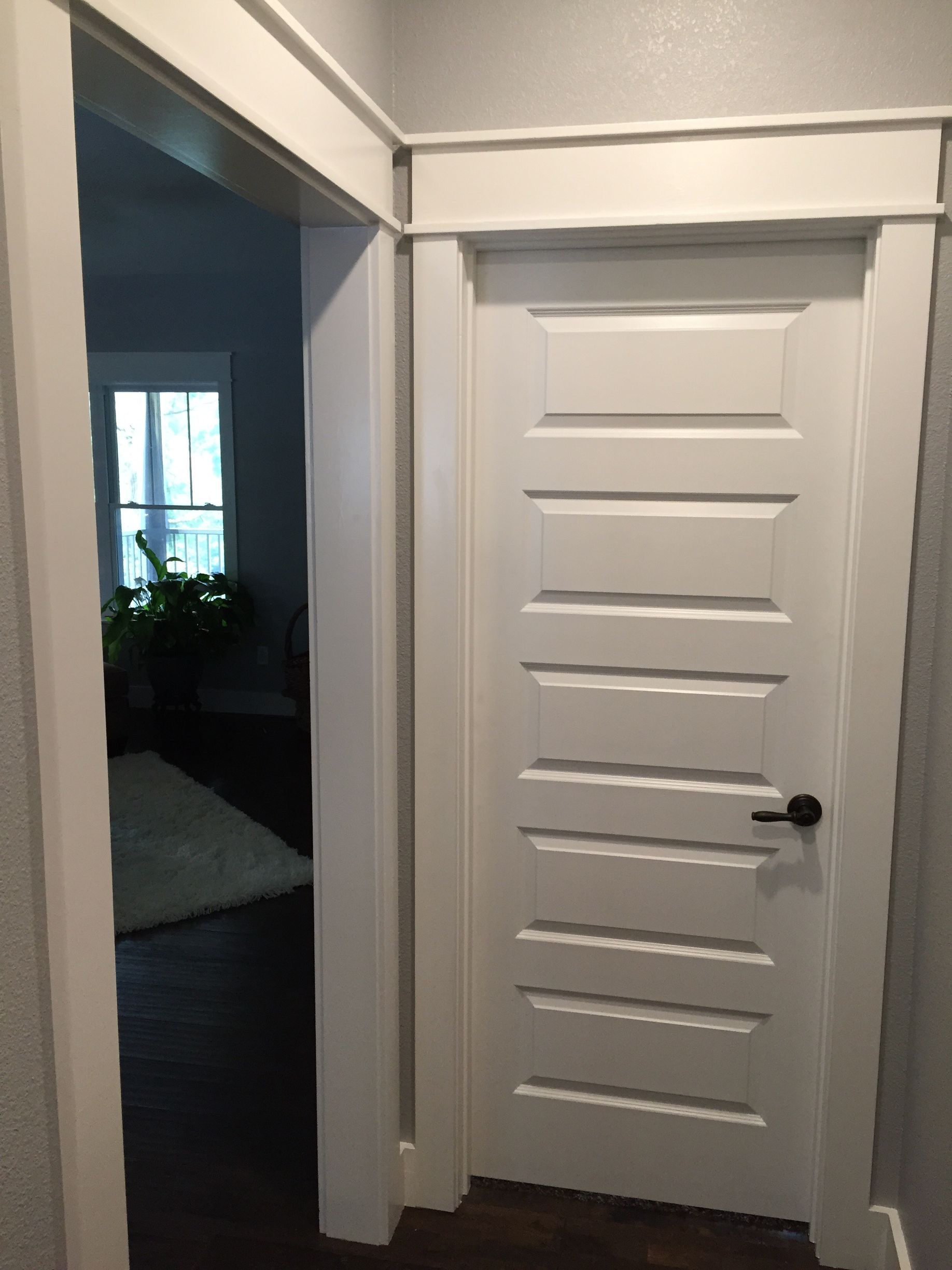 Narrow hallway with a white paneled door, open doorway to a dim room on the left