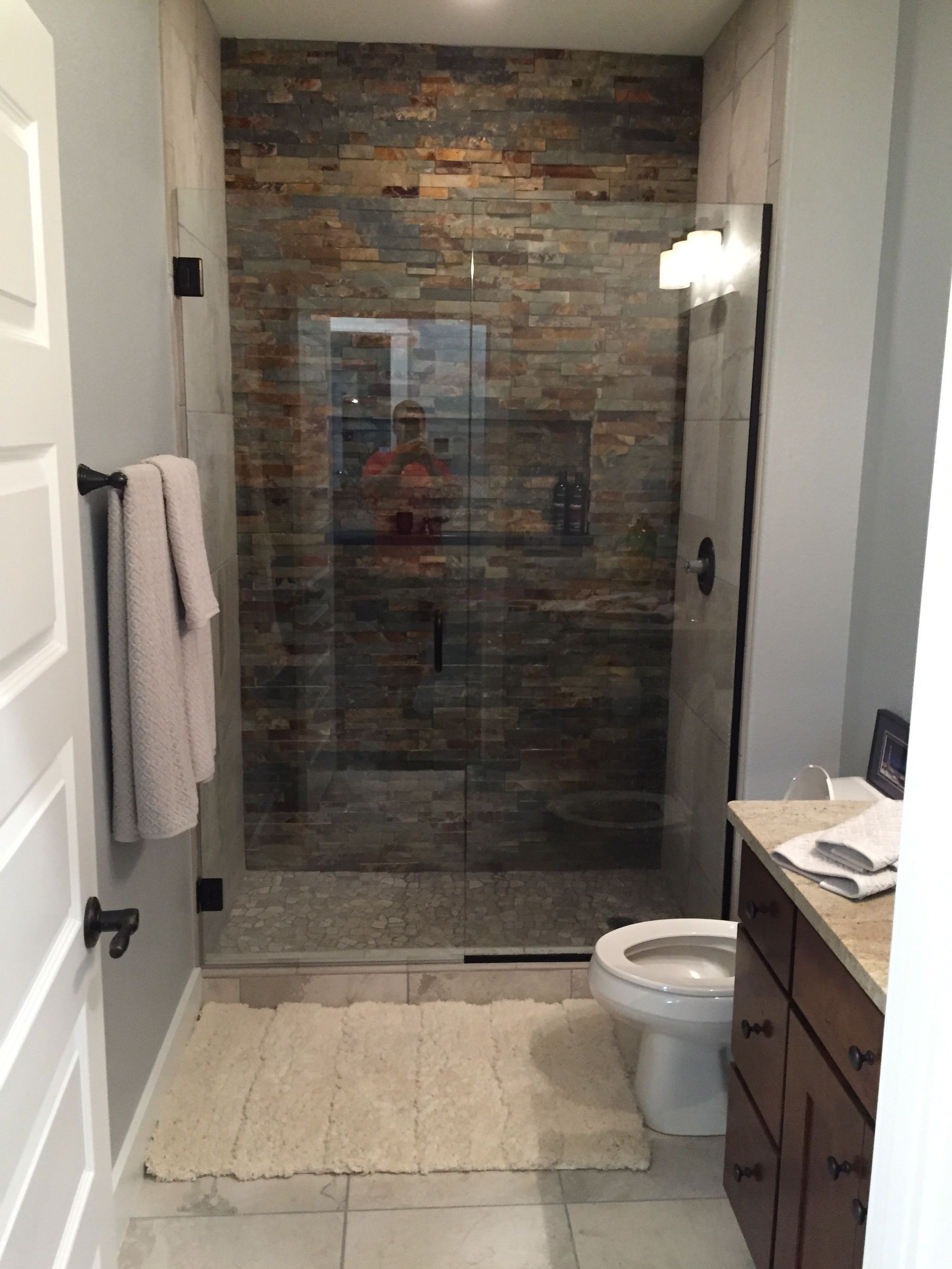Bathroom with glass shower, stone accent wall, white tub mat, and dark wood vanity.